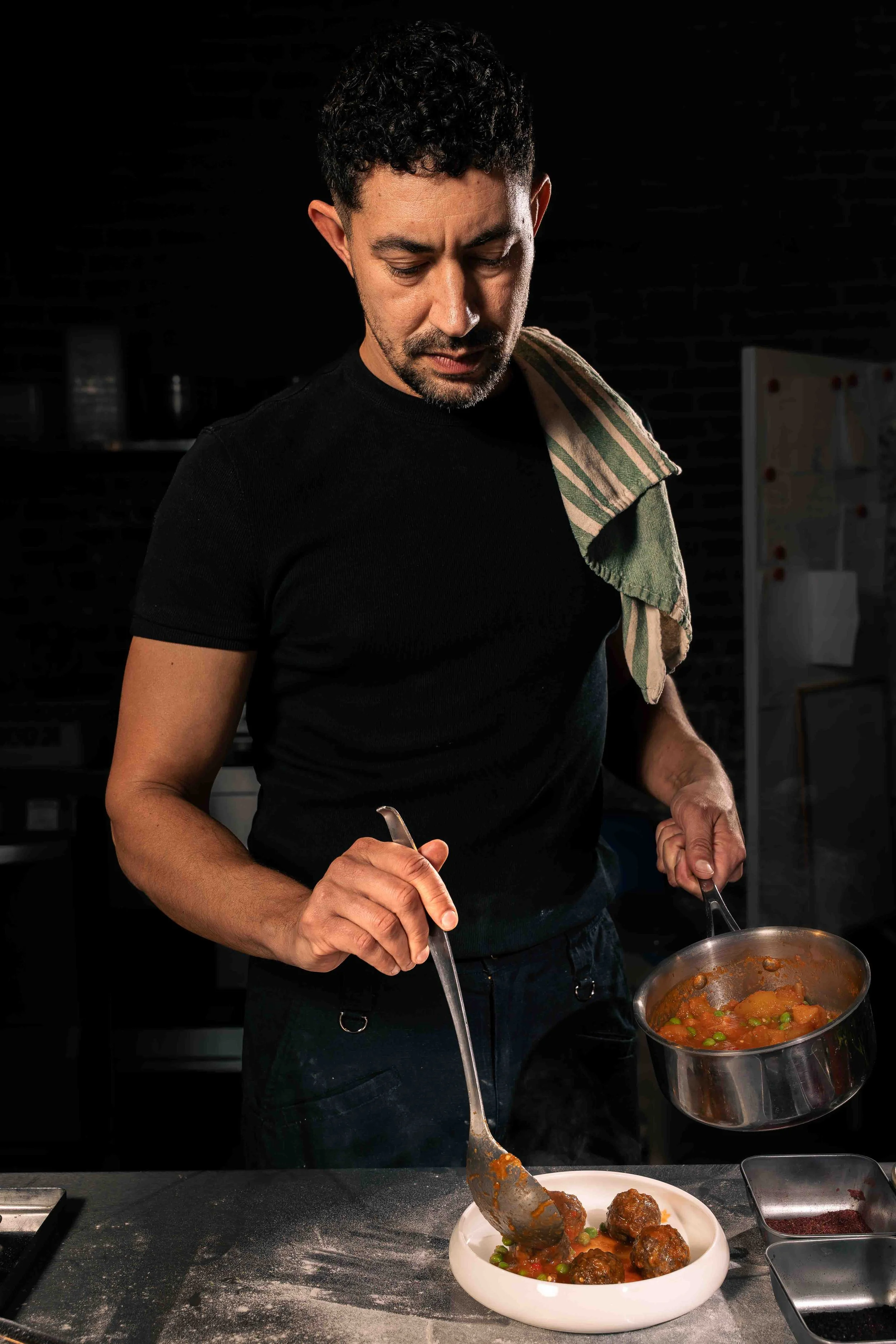 Photographie de portrait éditorial réalisée en cuisine, montrant un chef en train de dresser un plat avec précision. La lumière naturelle met en valeur les gestes, les textures et l’atmosphère du lieu dans une approche à la fois documentaire et const