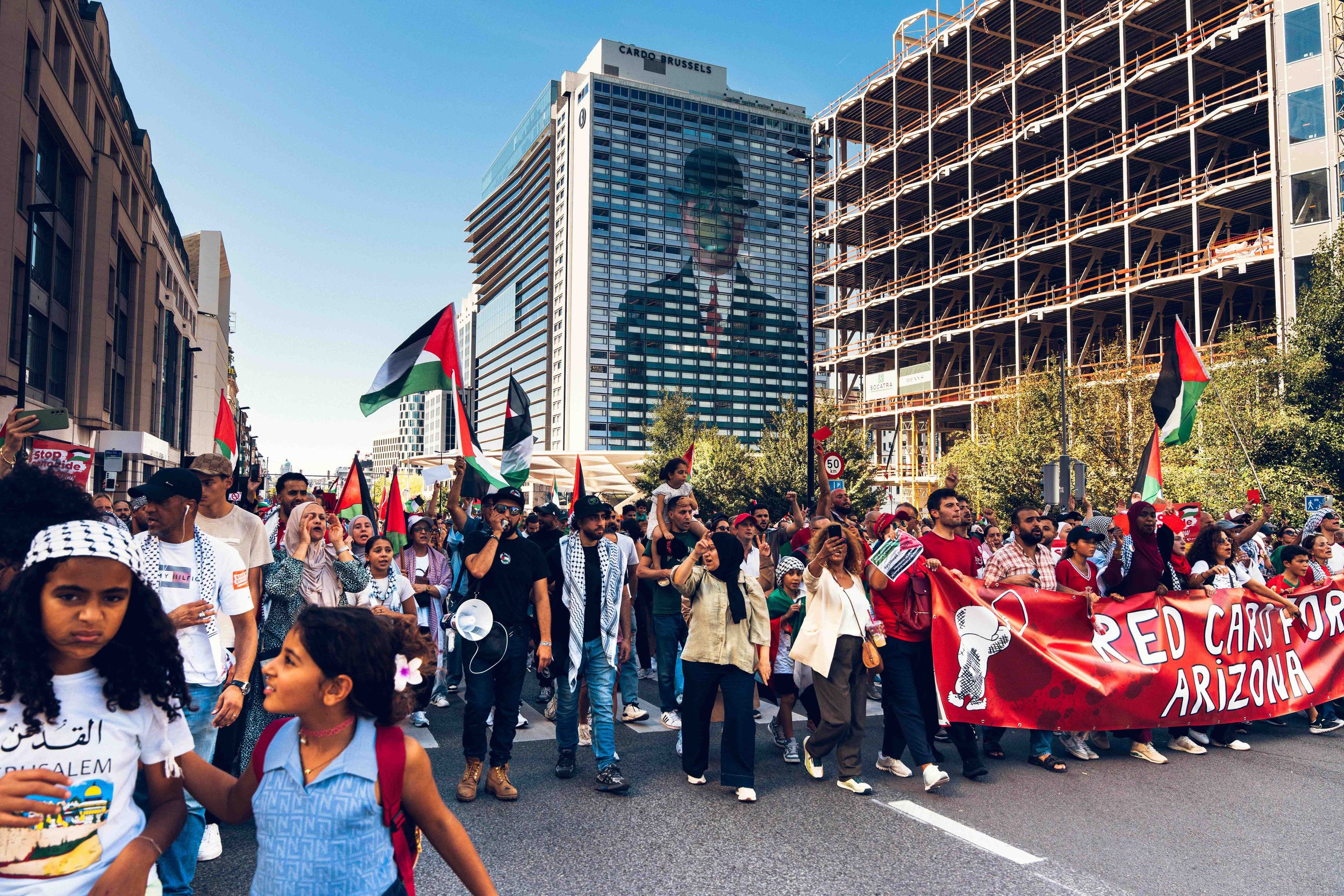 Photographie de reportage capturant une manifestation pro-palestinienne dans les rues de Bruxelles. Une foule de manifestants avance en brandissant des drapeaux palestiniens et des banderoles, exprimant leur soutien lors d’un rassemblement public. L’