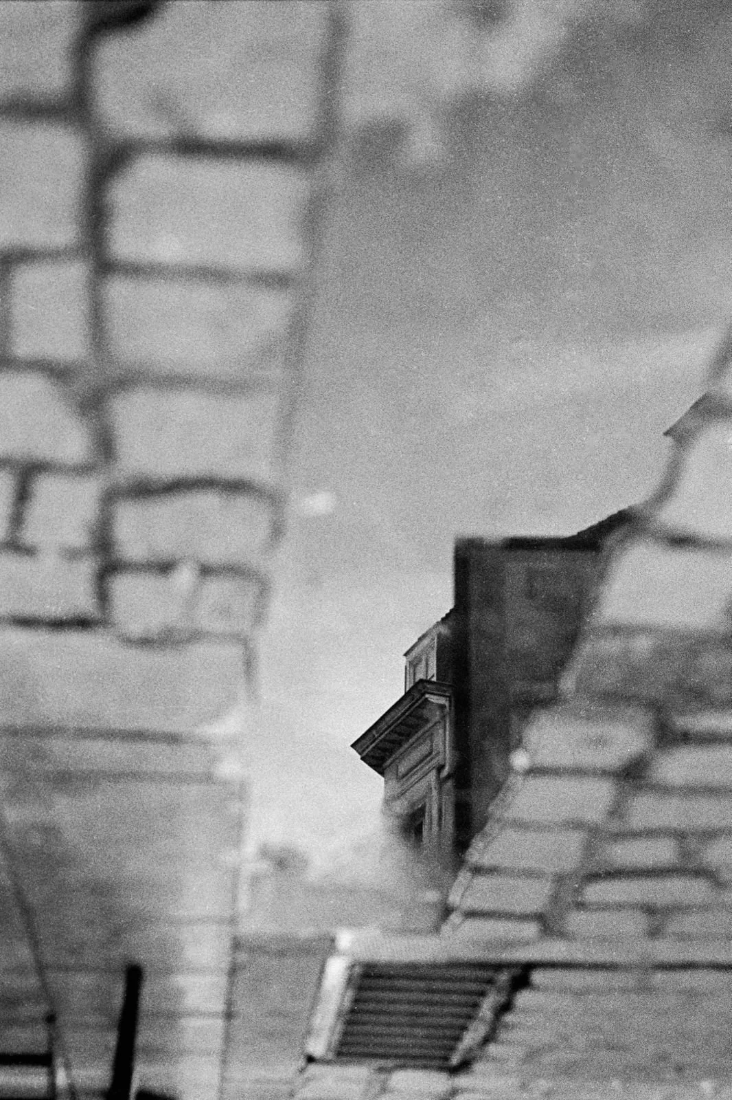 Photographie d'architecture en noir et blanc montrant le reflet d'un immeuble dans une flaque d'eau, avec une composition abstraite réalisée à Bruxelles.