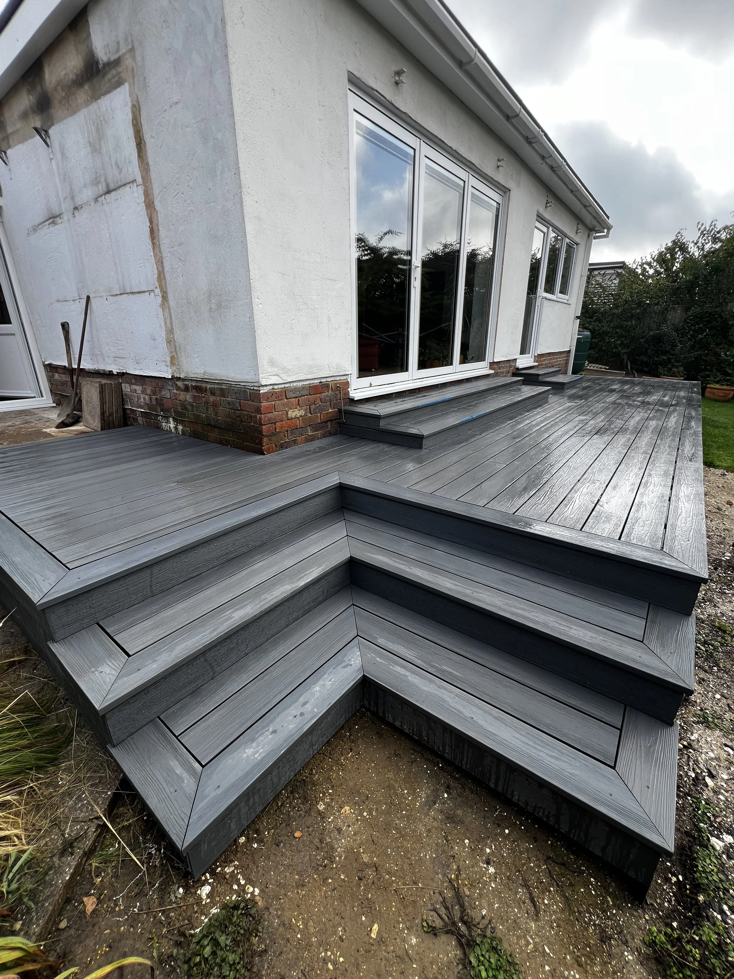 Newly constructed wooden deck with multiple steps attached to the back of a house with sliding glass doors.