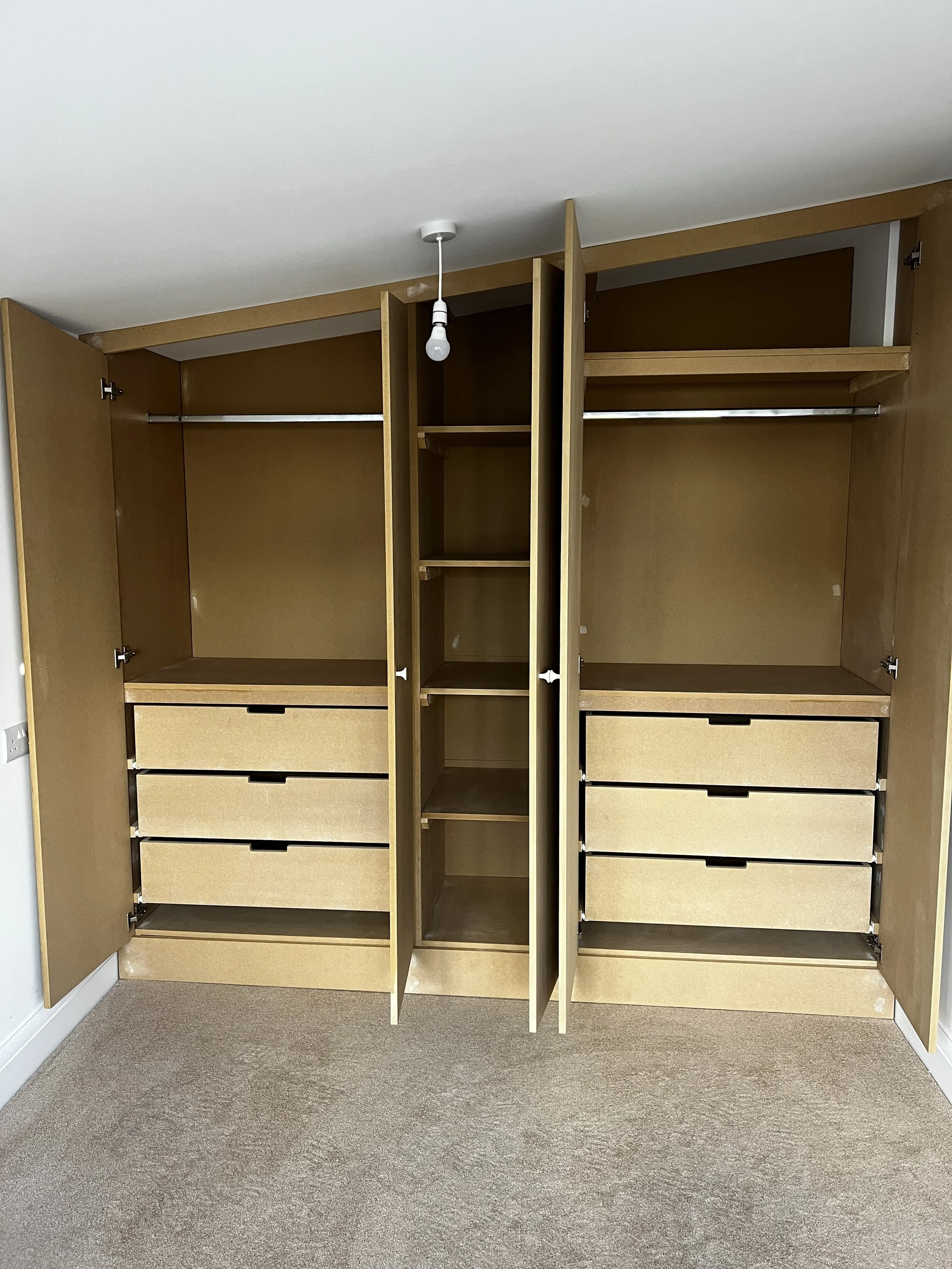 Empty wooden wardrobe with open doors, including drawers and shelves for clothing storage, on a beige carpeted floor.