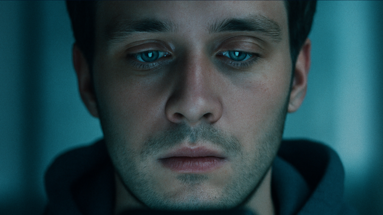 Das Bild zeigt eine Nahaufnahme einer männlich gelesene Person mit müdem Gesichtsausdruck, die auf ein Handy starrt. Das Handy selbst ist nur die Reflexion des Screens in den Augen der Person zu erahnen.