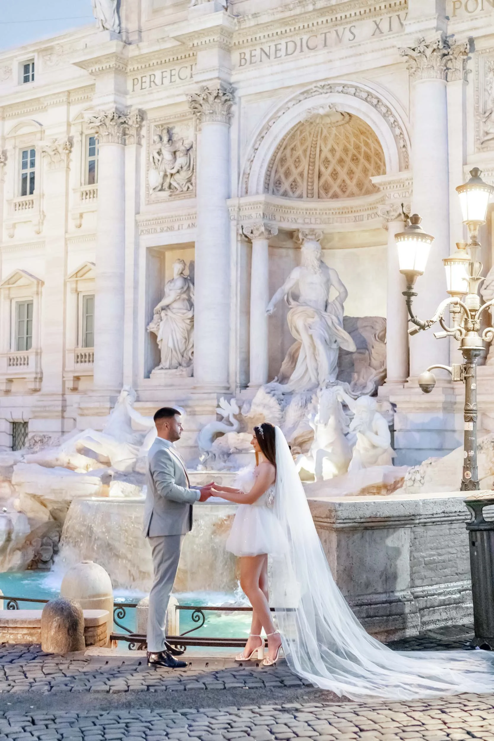 A bride and groom holding hands in front of the Trevi Fountain in Rome during their wedding ceremony.