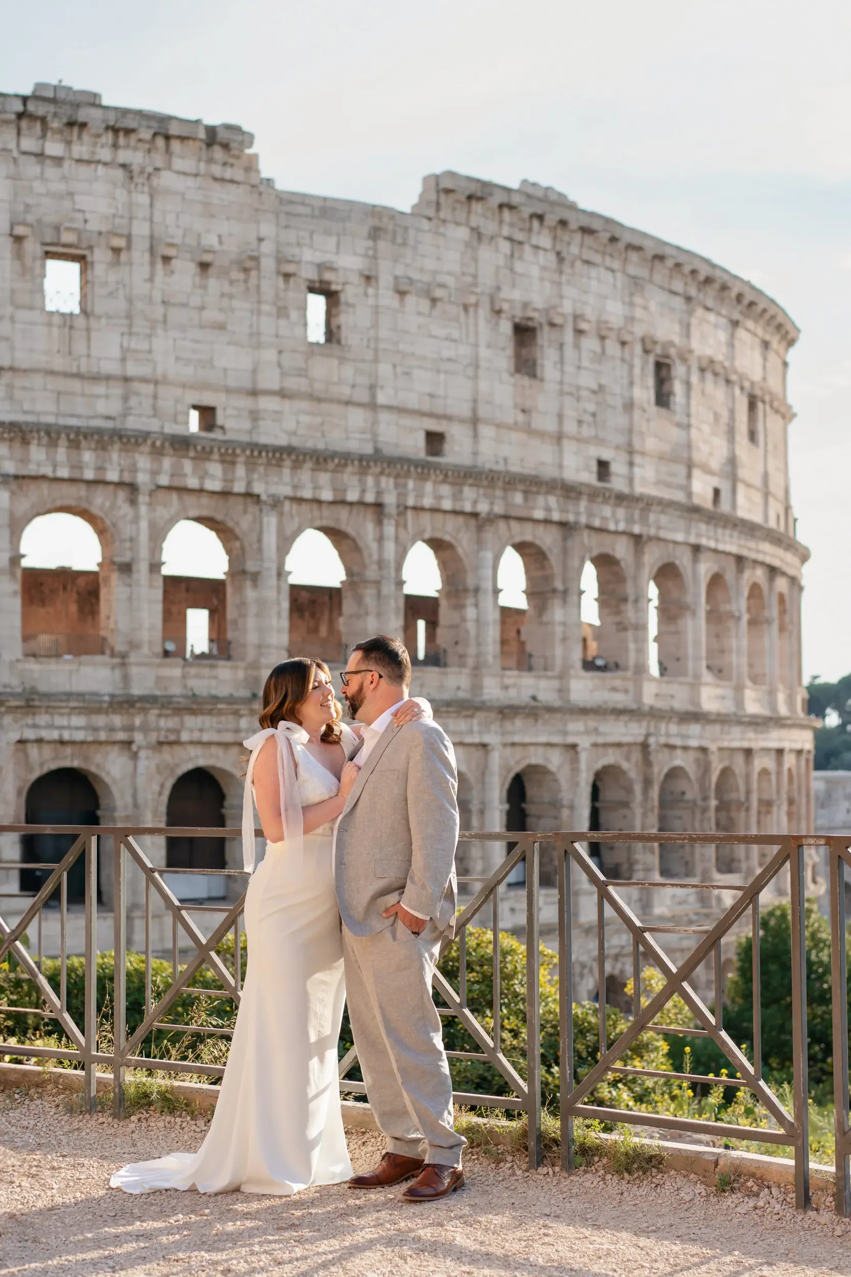 A couple in wedding attire looking at each other in front of the Roman Colosseum.