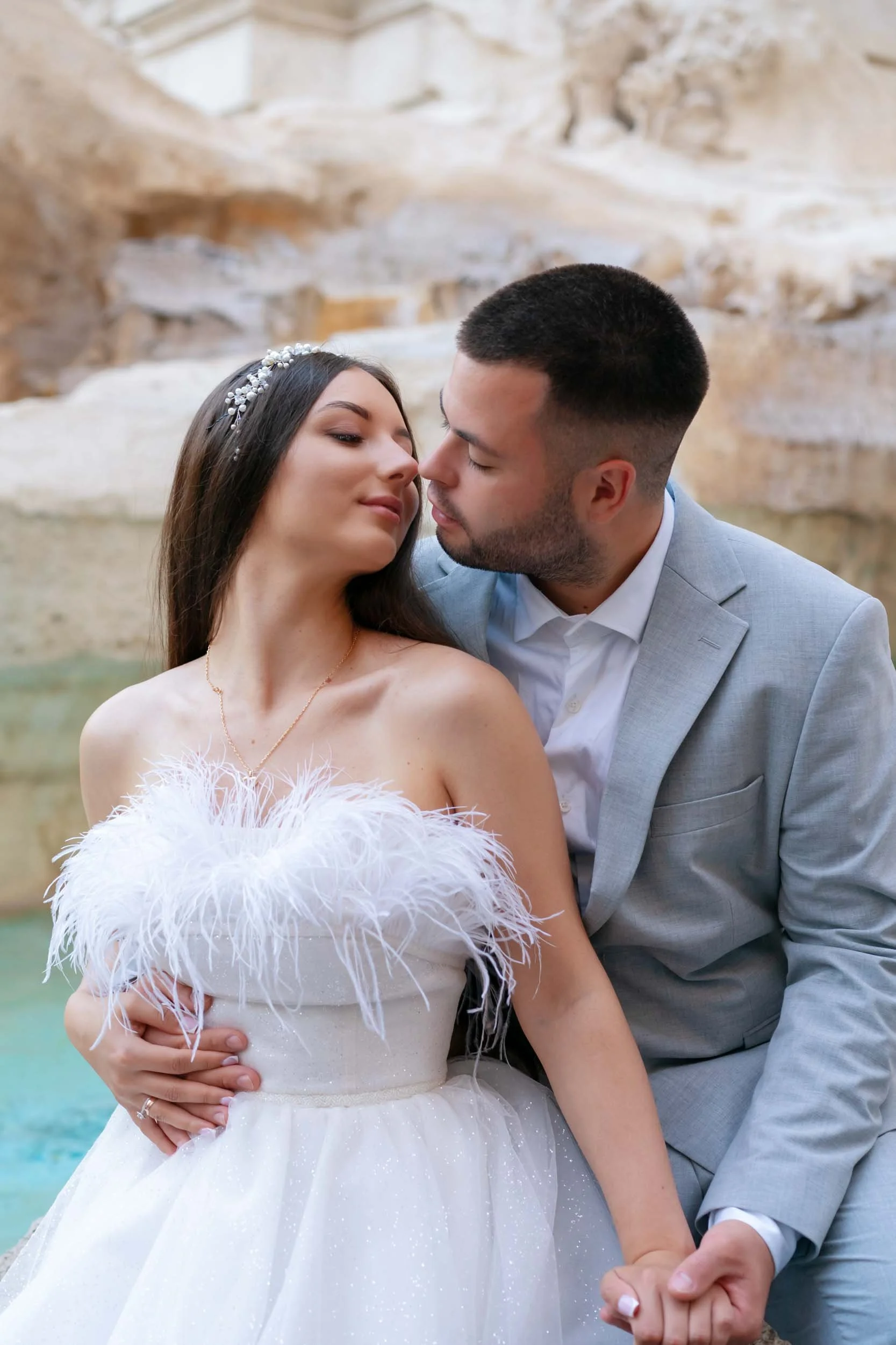 A bride and groom sharing an intimate moment against a rocky background, with the groom holding the bride's waist and their faces close together.