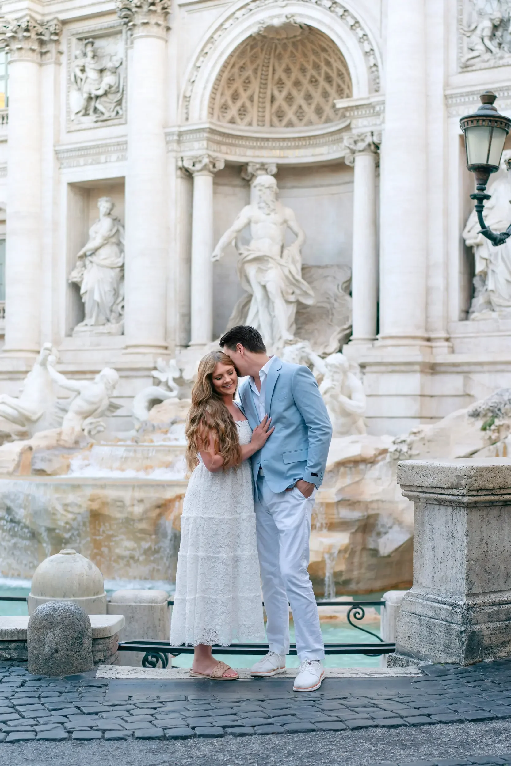 A couple in formal attire sharing a kiss in front of the Trevi Fountain in Rome, Italy.