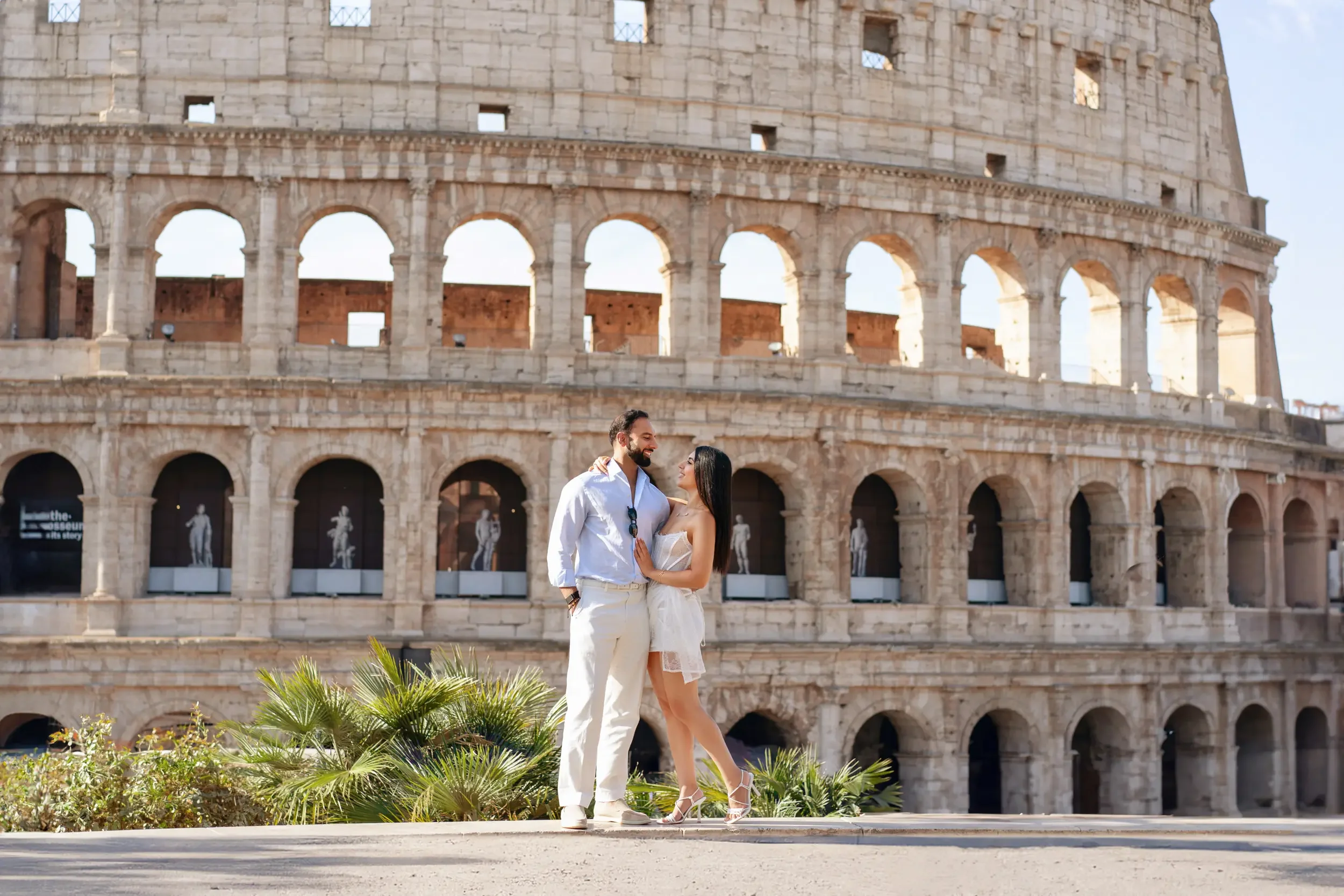 A couple standing in front of the Roman Colosseum, embracing each other and smiling.