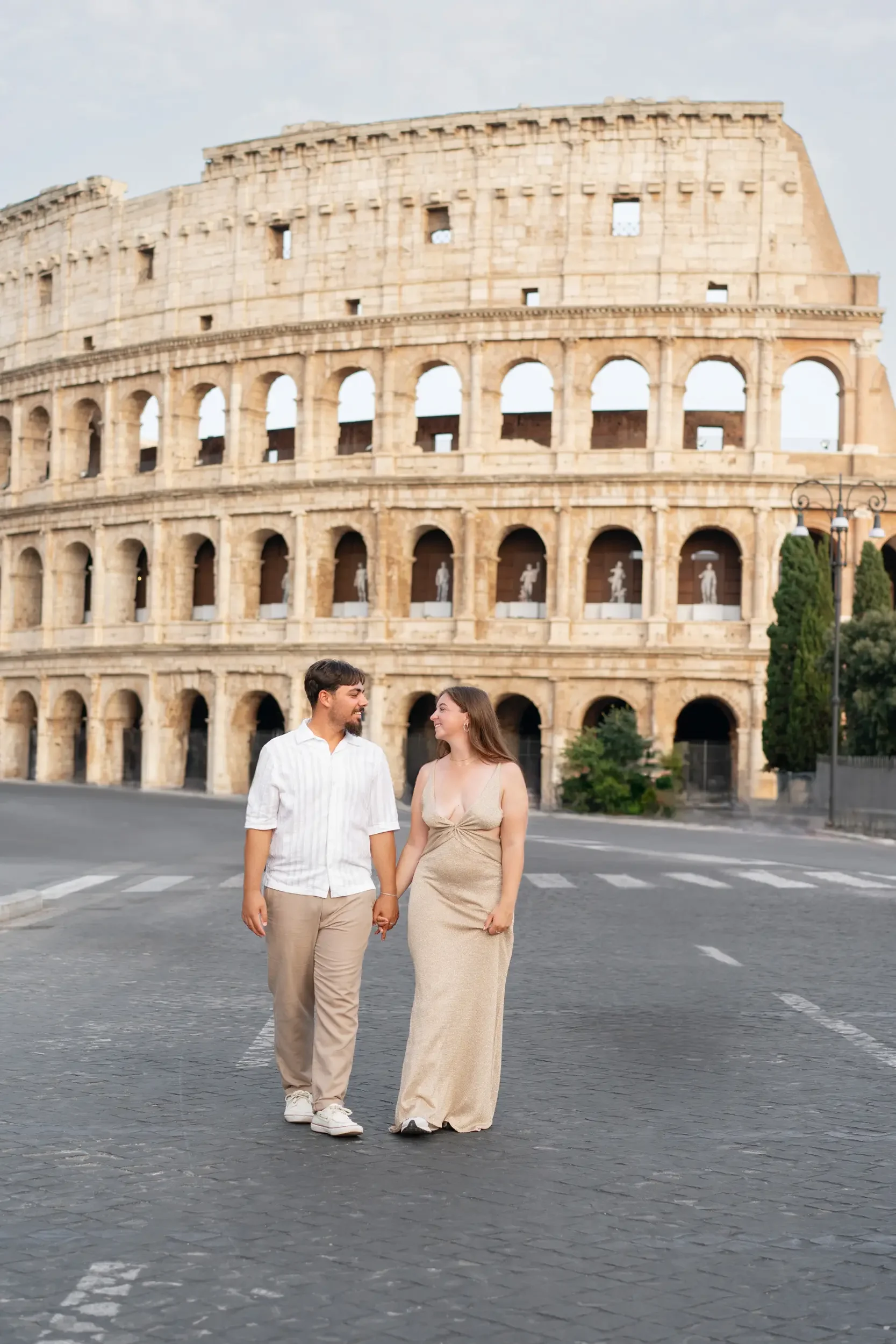 A couple holding hands and smiling while walking on a street in front of the Roman Colosseum.