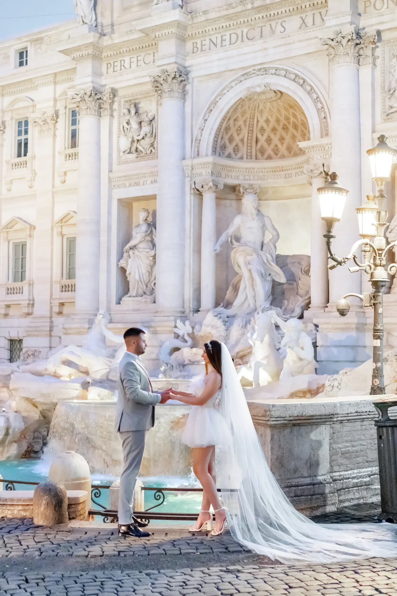A bride and groom holding hands in front of the Trevi Fountain in Rome, Italy, during their wedding.