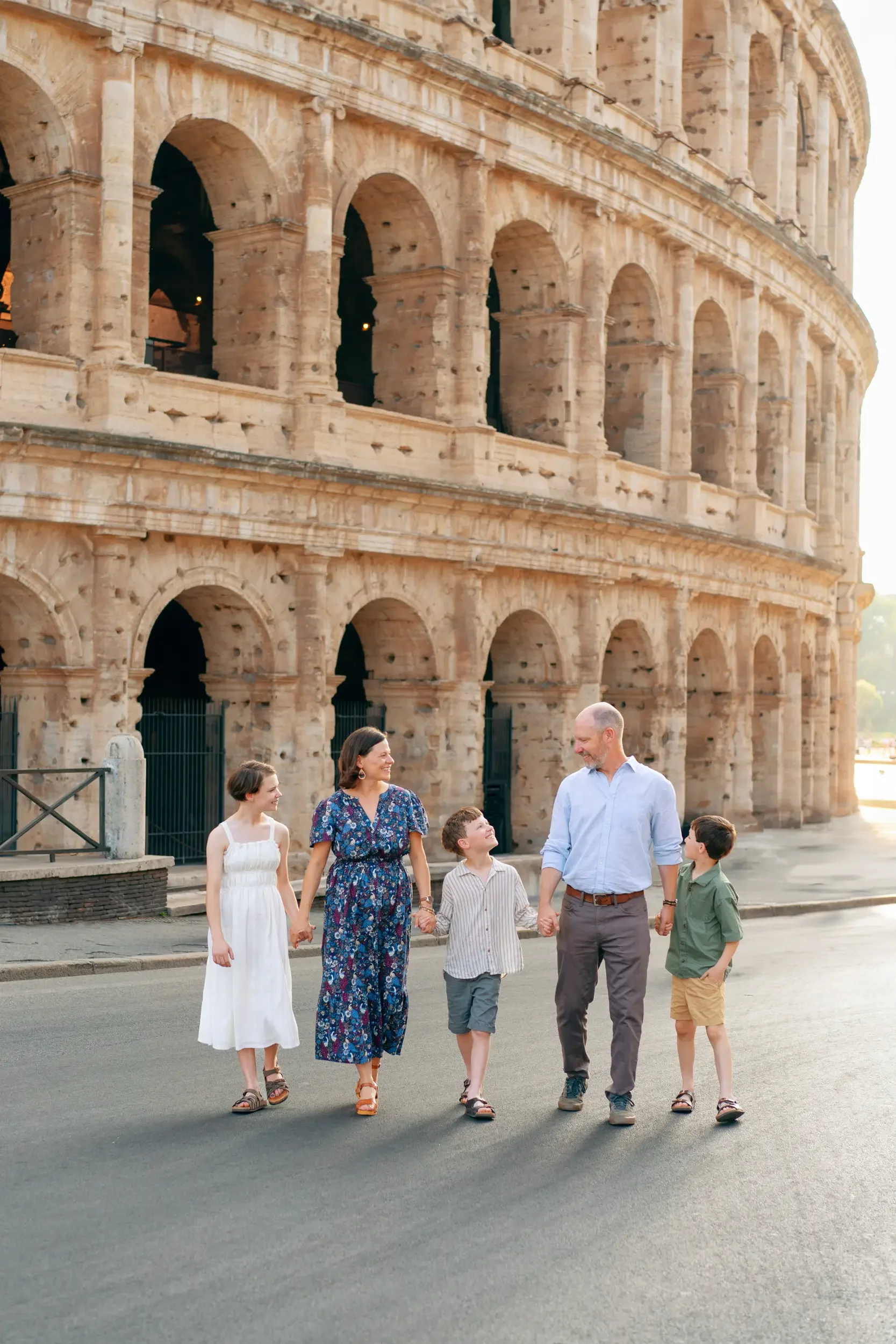 Family of five walking in front of the Colosseum in Rome, Italy, holding hands and smiling during sunset.