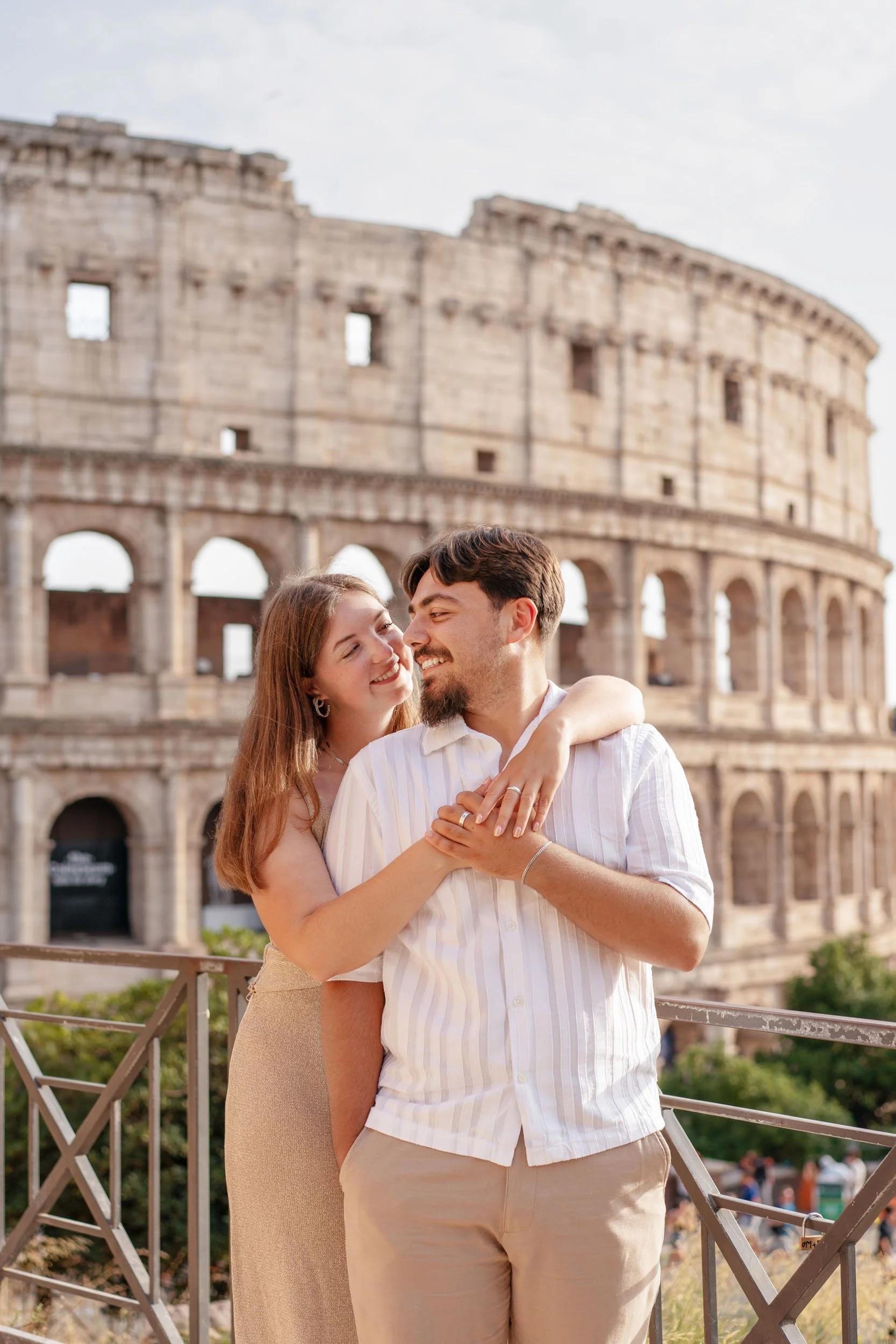 A young couple hugging and smiling in front of the Colosseum in Rome, Italy.
