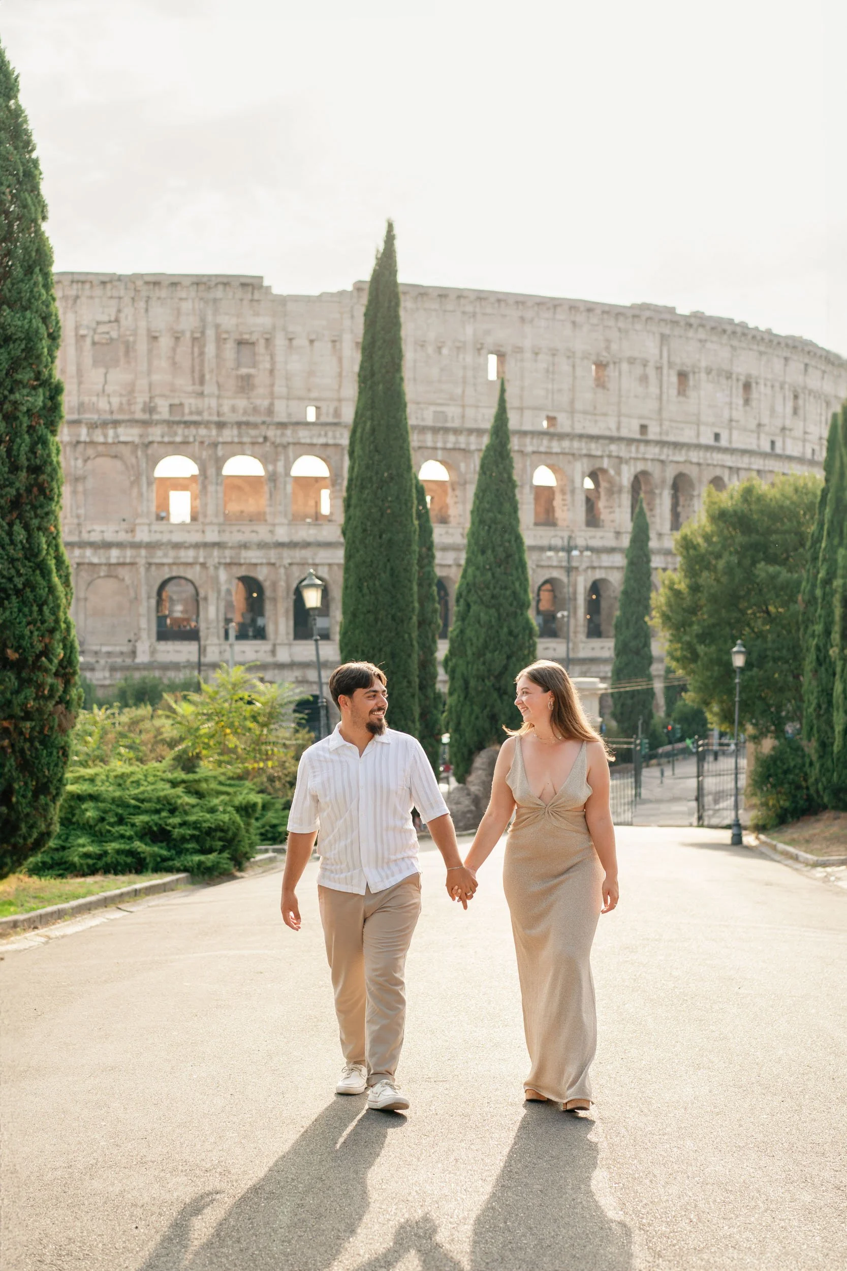 A couple holding hands and walking in front of the Colosseum in Rome, Italy, during daytime.