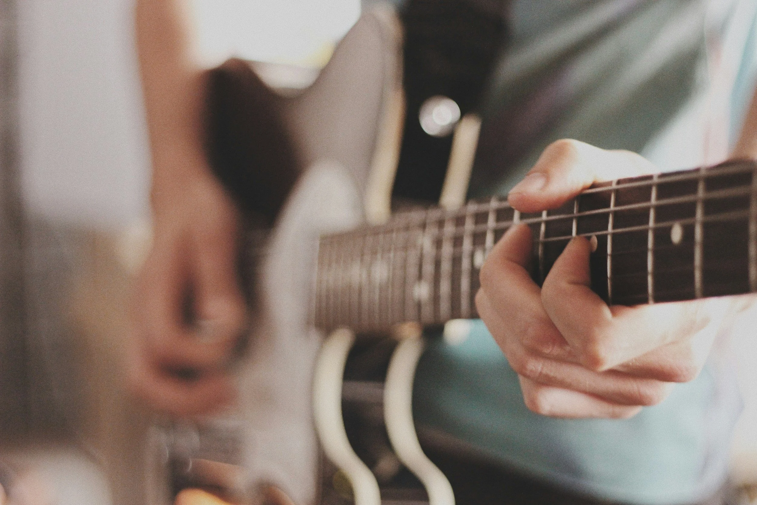 Person playing an acoustic guitar, focusing on their hand pressing the strings on the fretboard.