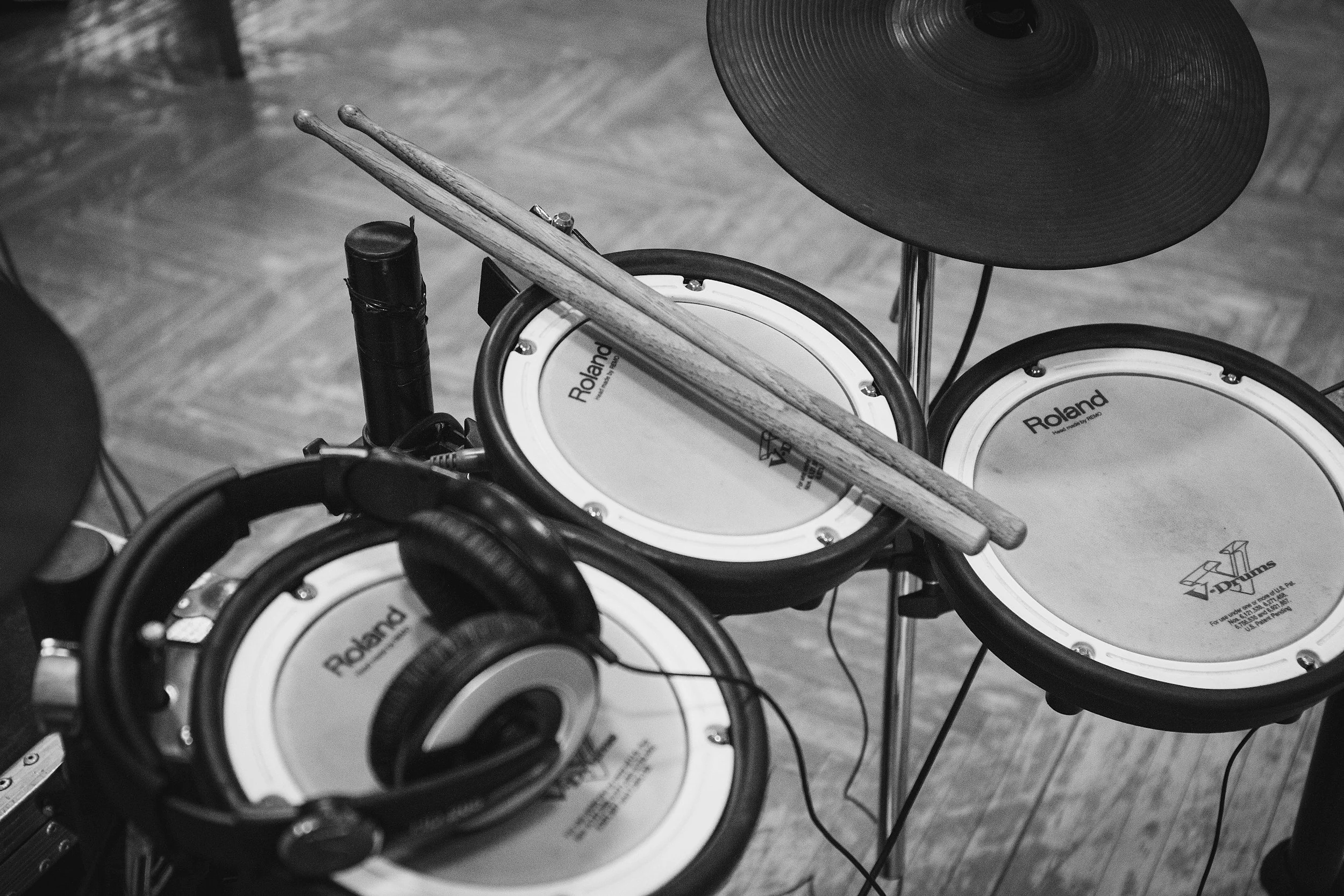 Black-and-white photo of a digital drum set with a pair of drumsticks resting on the drum surface and over the cymbal.