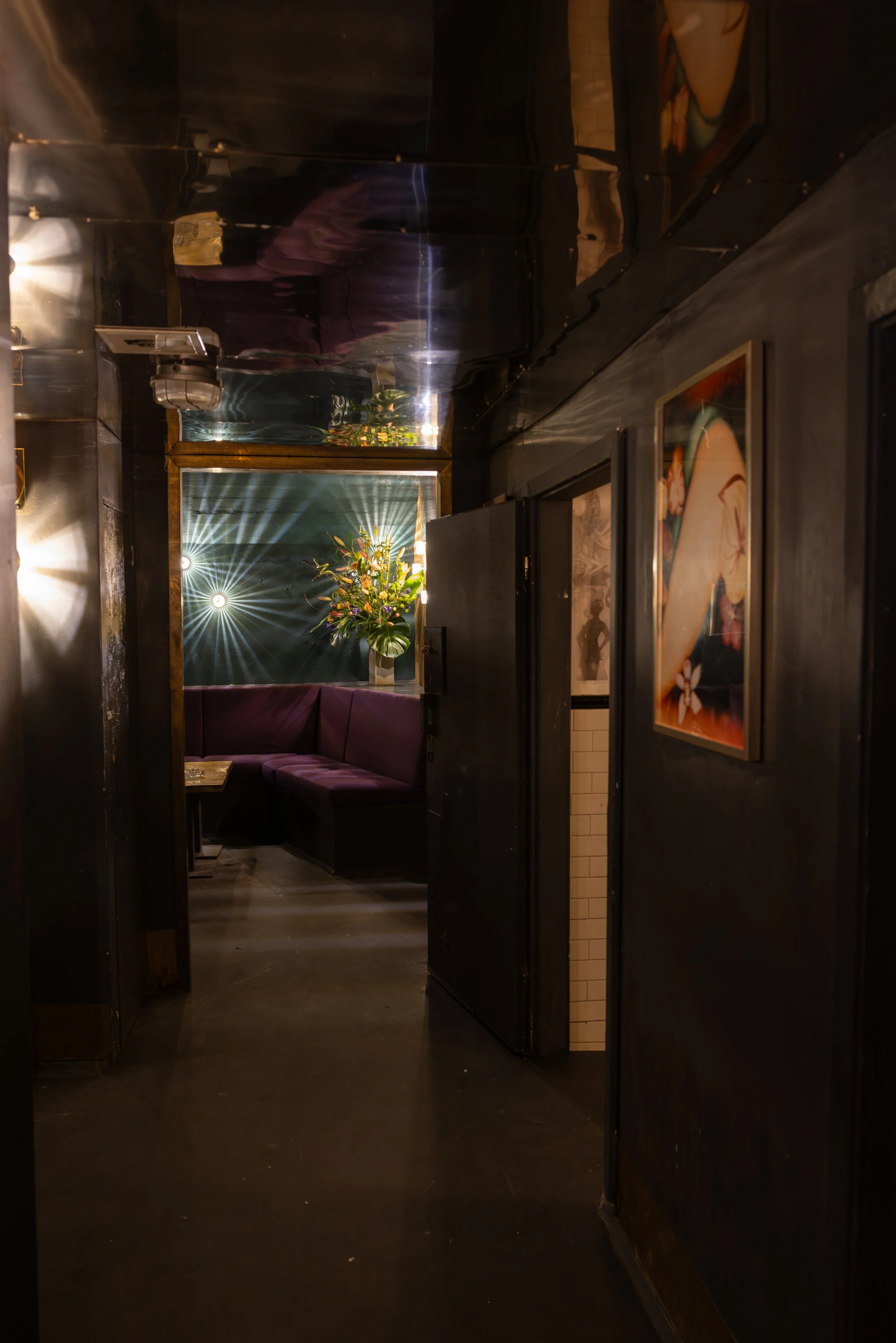 Dunkles Flur in einem Restaurant mit einer Sitznische, einer Blumenpflanze, Wandkunst und gedämpftem Licht.