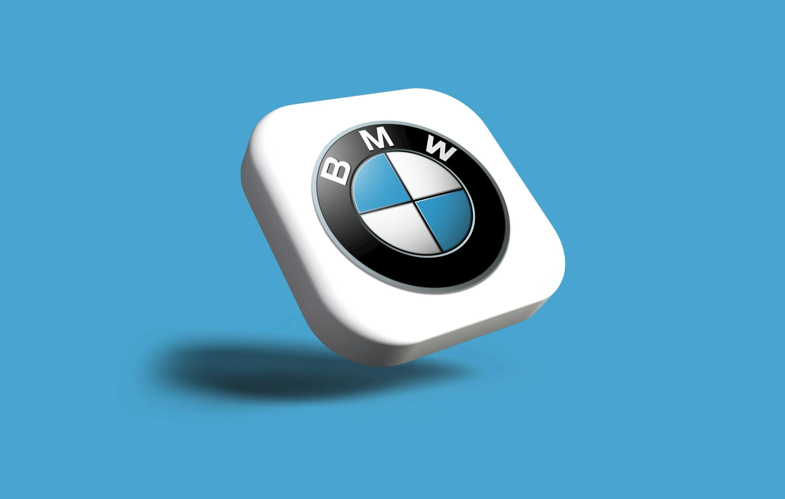 BMW Logo auf einem weißen, abgerundeten Objekt vor blauem Hintergrund, mit Schatten nach unten links.