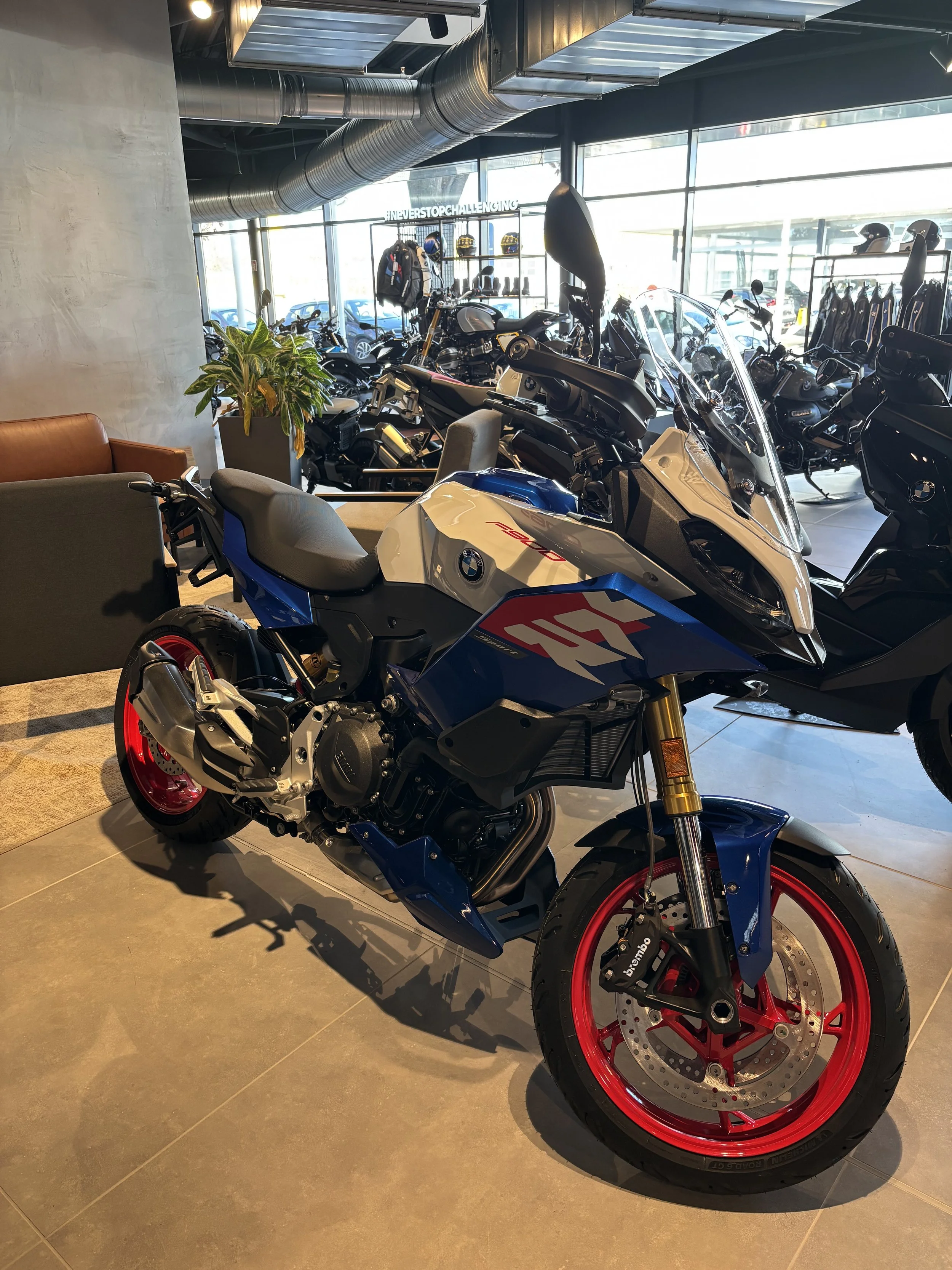BMW S 1000 XR Motorrad im Motorradgeschäft mit weiteren Motorrädern im Hintergrund, große Fenster, moderne Inneneinrichtung, Deko-Pflanze, komfortabler Sitzbereich.