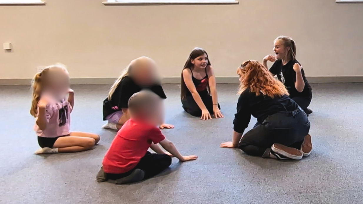 Children sitting in a circle on the floor with their teacher during a confidence-building drama class in Farndon
