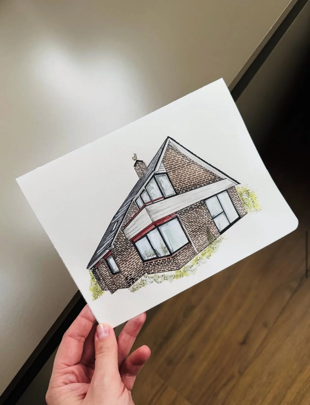 Hand holding a sketch of a modern house with brick walls and large windows.