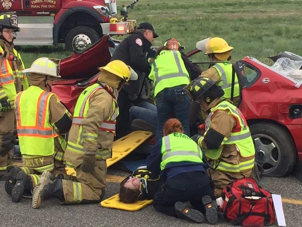 Firefighters and emergency responders attending to a car accident involving a red sports car.