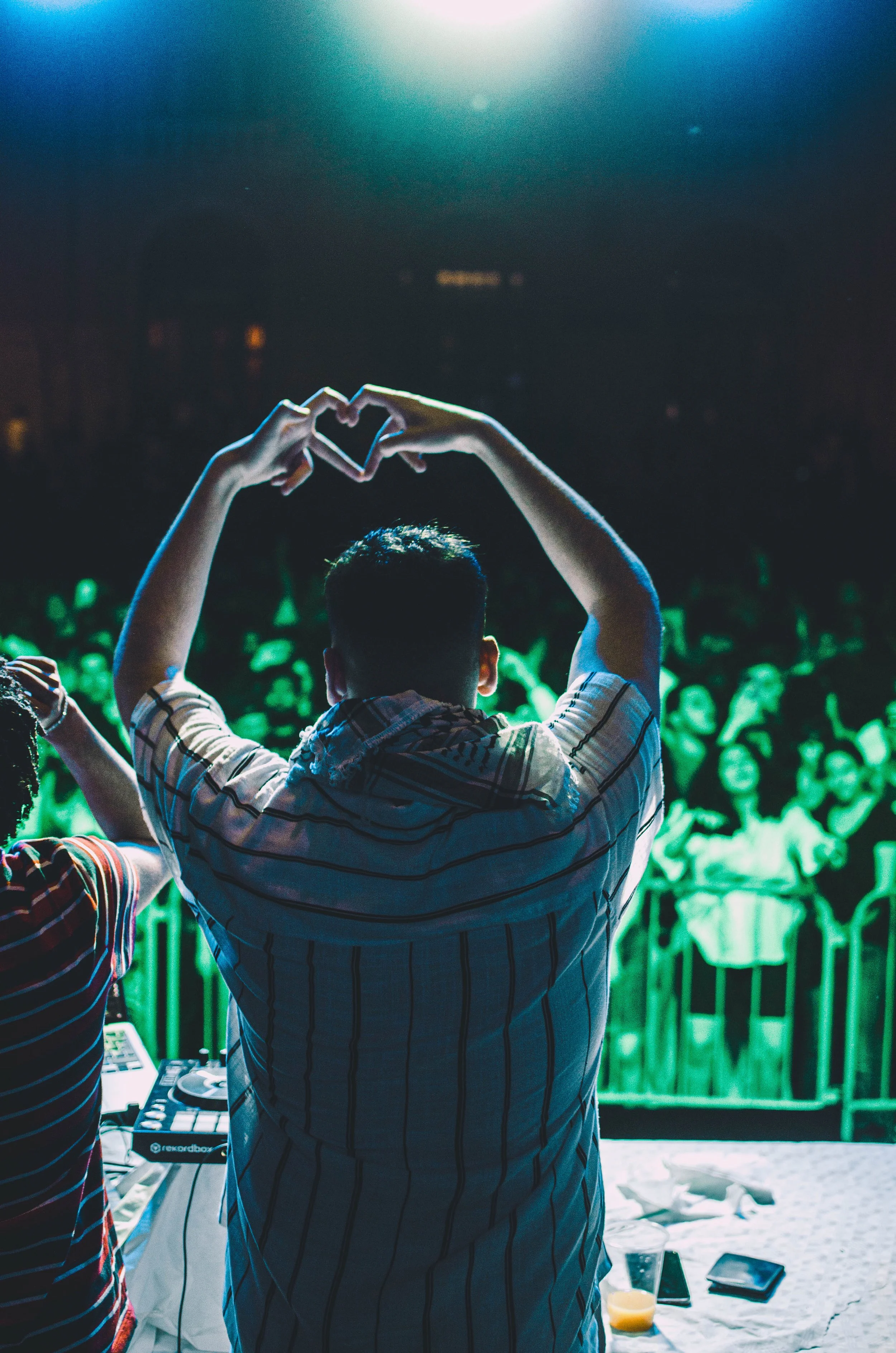 Person on stage with hands in heart shape and a heart made with fingers, facing a crowd at night.