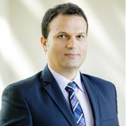 Professional man in a suit with a blue tie, posing for a portrait with a neutral background.