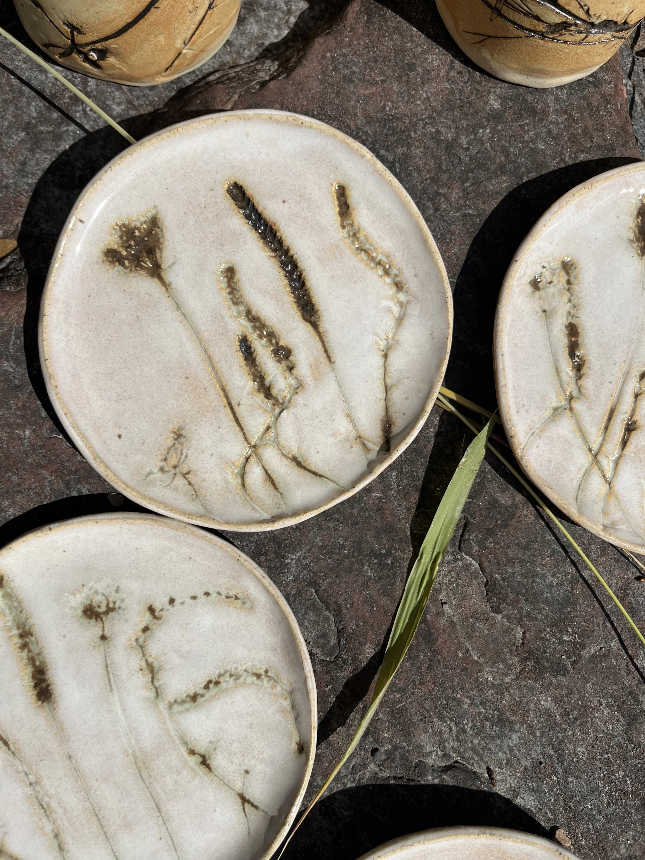 Ceramic plates with dried grass designs, resting on a stone surface.