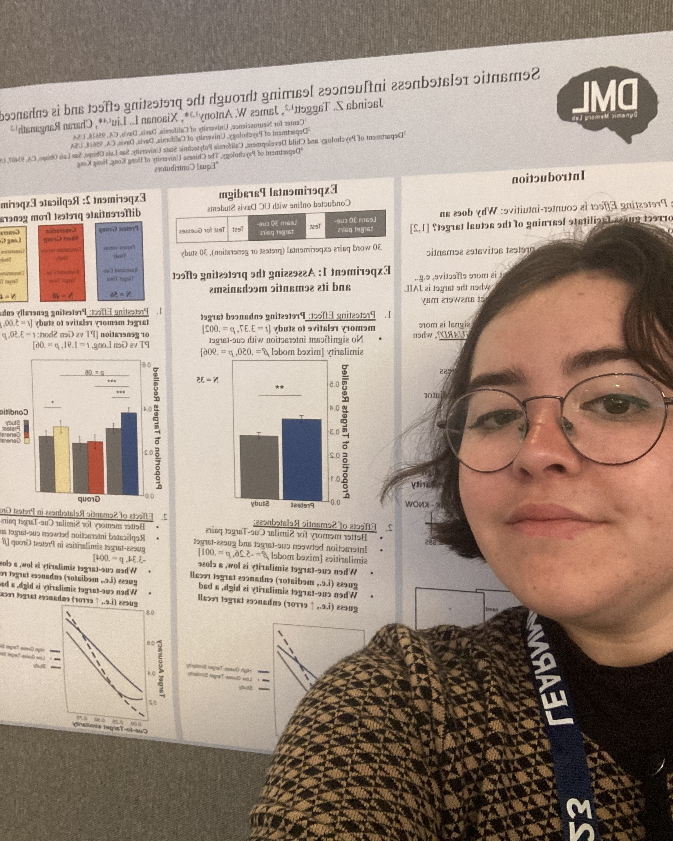 Person wearing glasses and a patterned jacket taking a selfie next to a scientific research poster containing graphs and text.