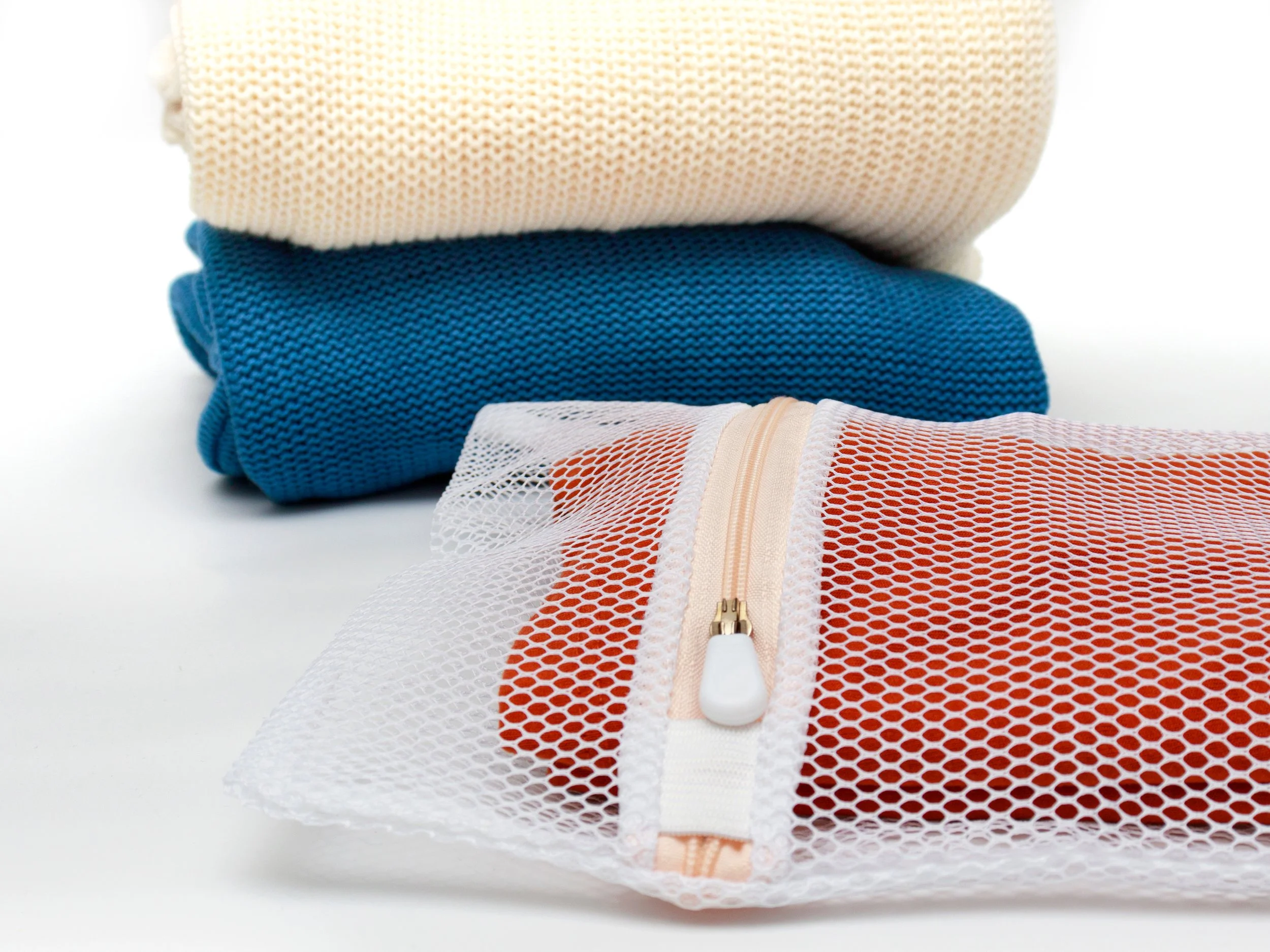 Stacked folded clothing and a mesh cosmetic bag with a zipper on a white background.