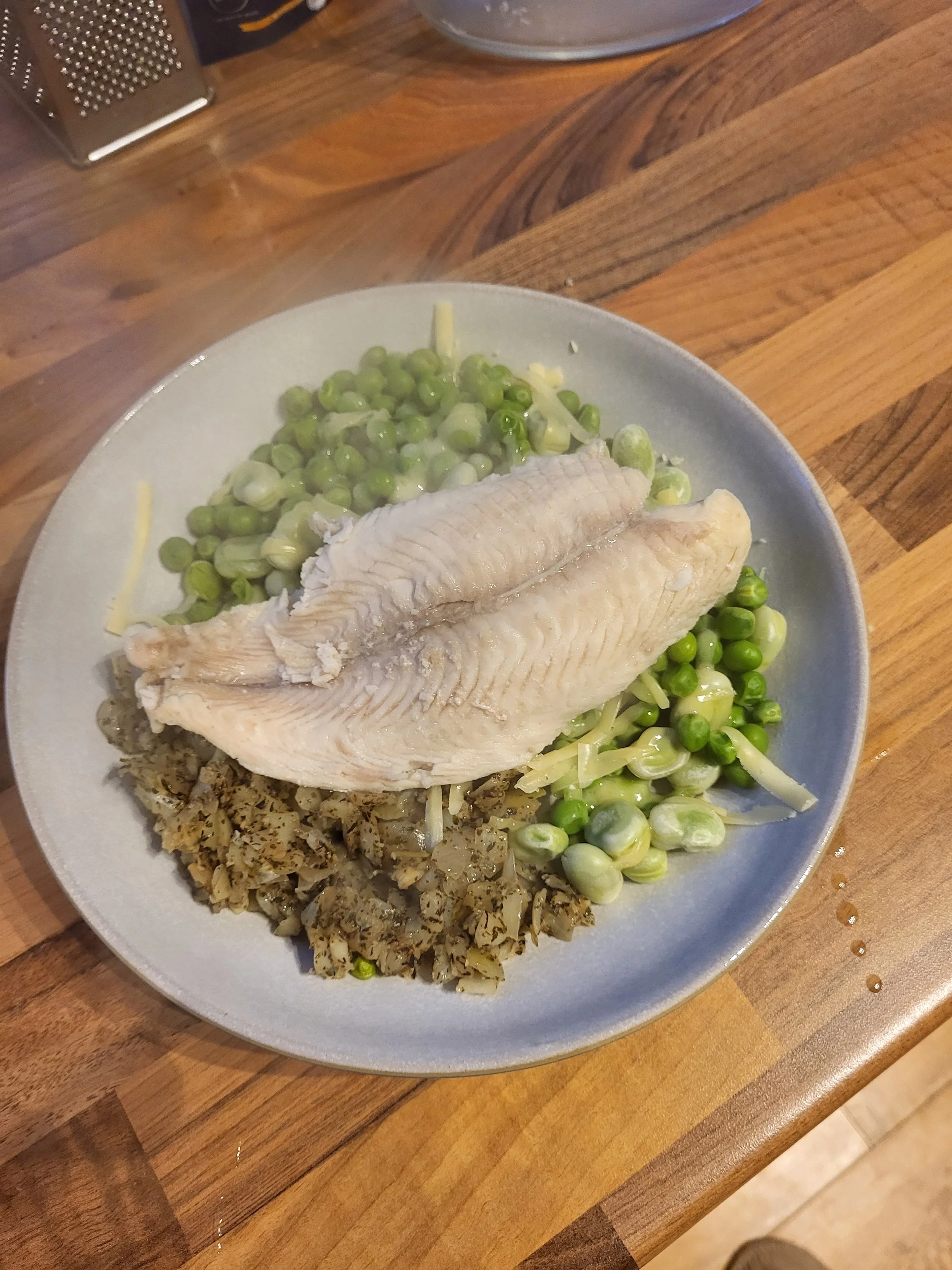Baked white fish fillet served with a side of green peas and chopped herbs on a plate.