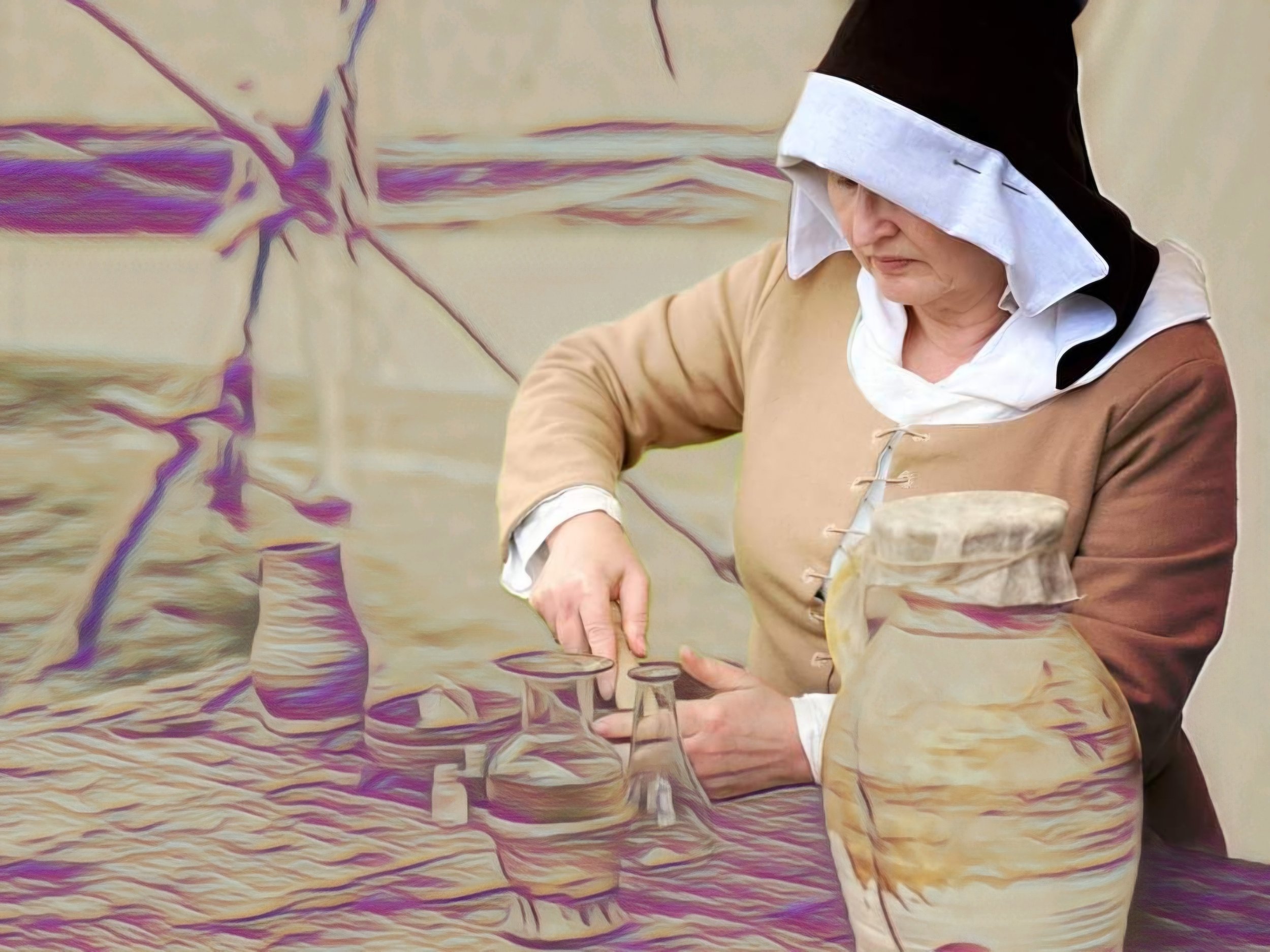 A female reenactor wearing 15th century clothing is using a pestle and mortar on a table that has various bottles and pottery