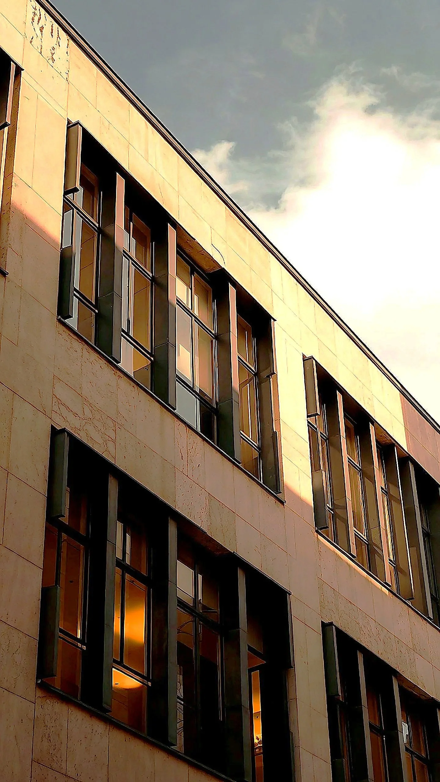Modernes Mehrfamilienhaus mit großen Fenstern bei Sonnenuntergang, blauer Himmel mit Wolken.