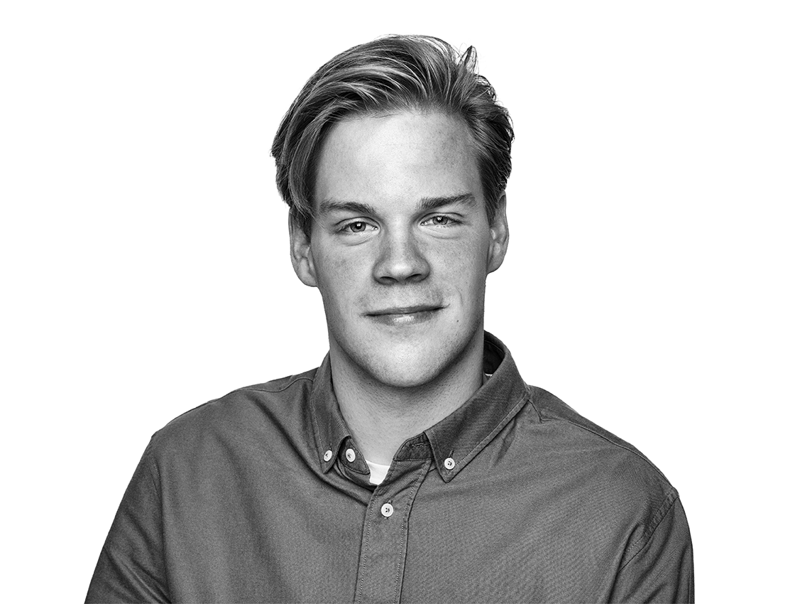 Zwart-wit portret van een jonge man met licht haar, een overhemd met kraag dragend, licht glimlachend tegen een effen witte achtergrond.