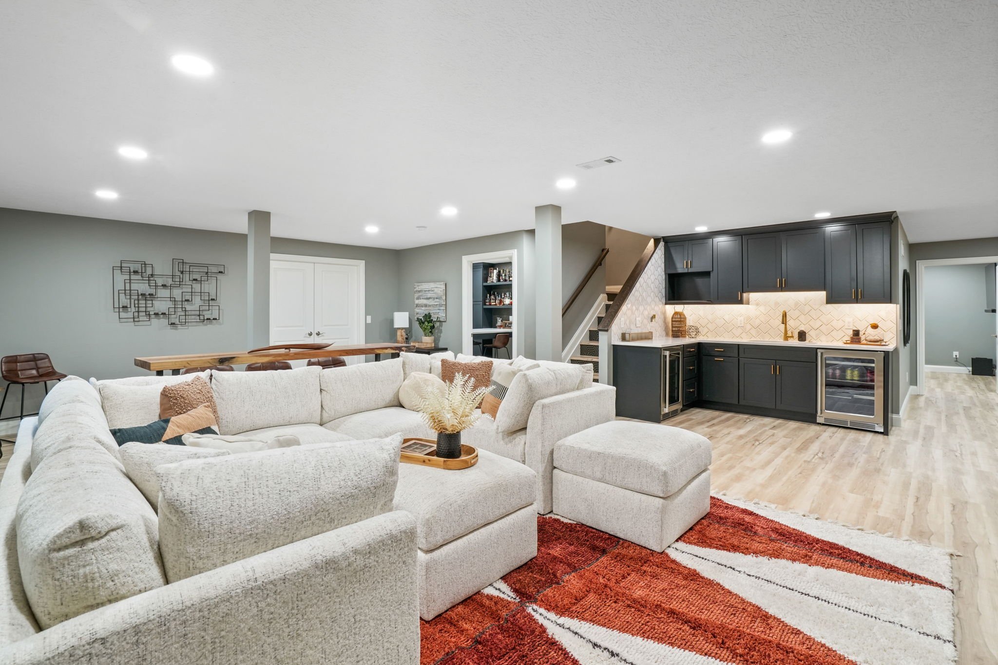 Open-concept living room with white sectional sofa, red area rug, and modern kitchen with dark cabinets and white backsplash.