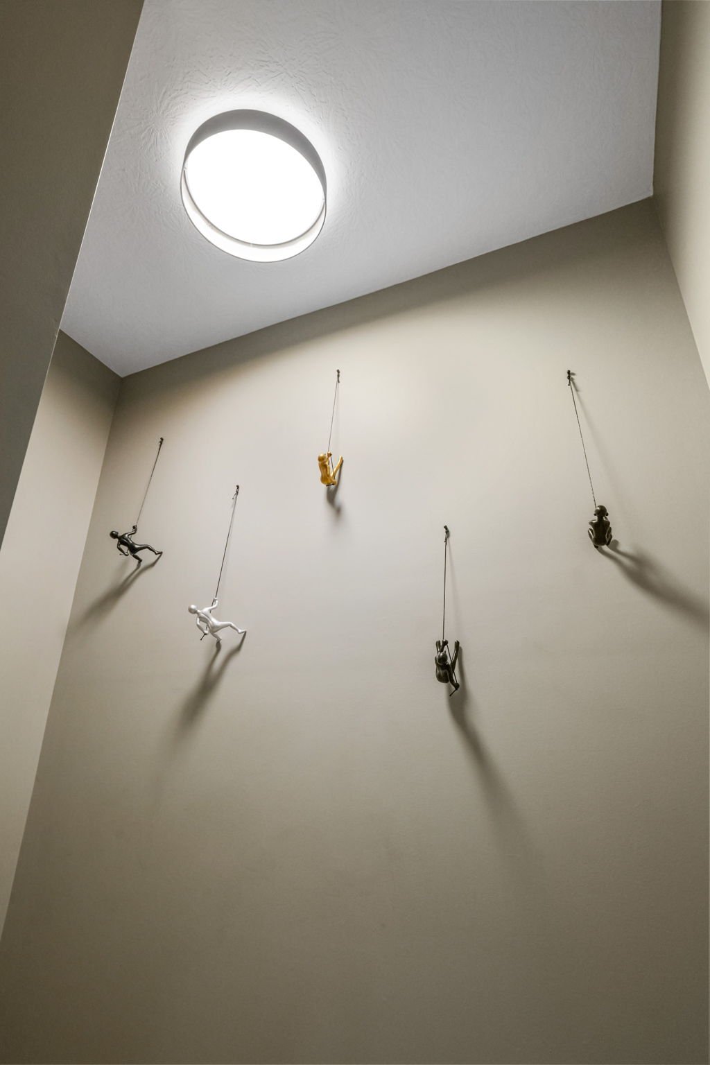 Indoor wall with small suspended figurines, including a monkey, a frog, and several other animals or characters, hanging from strings, with a circular ceiling light overhead.