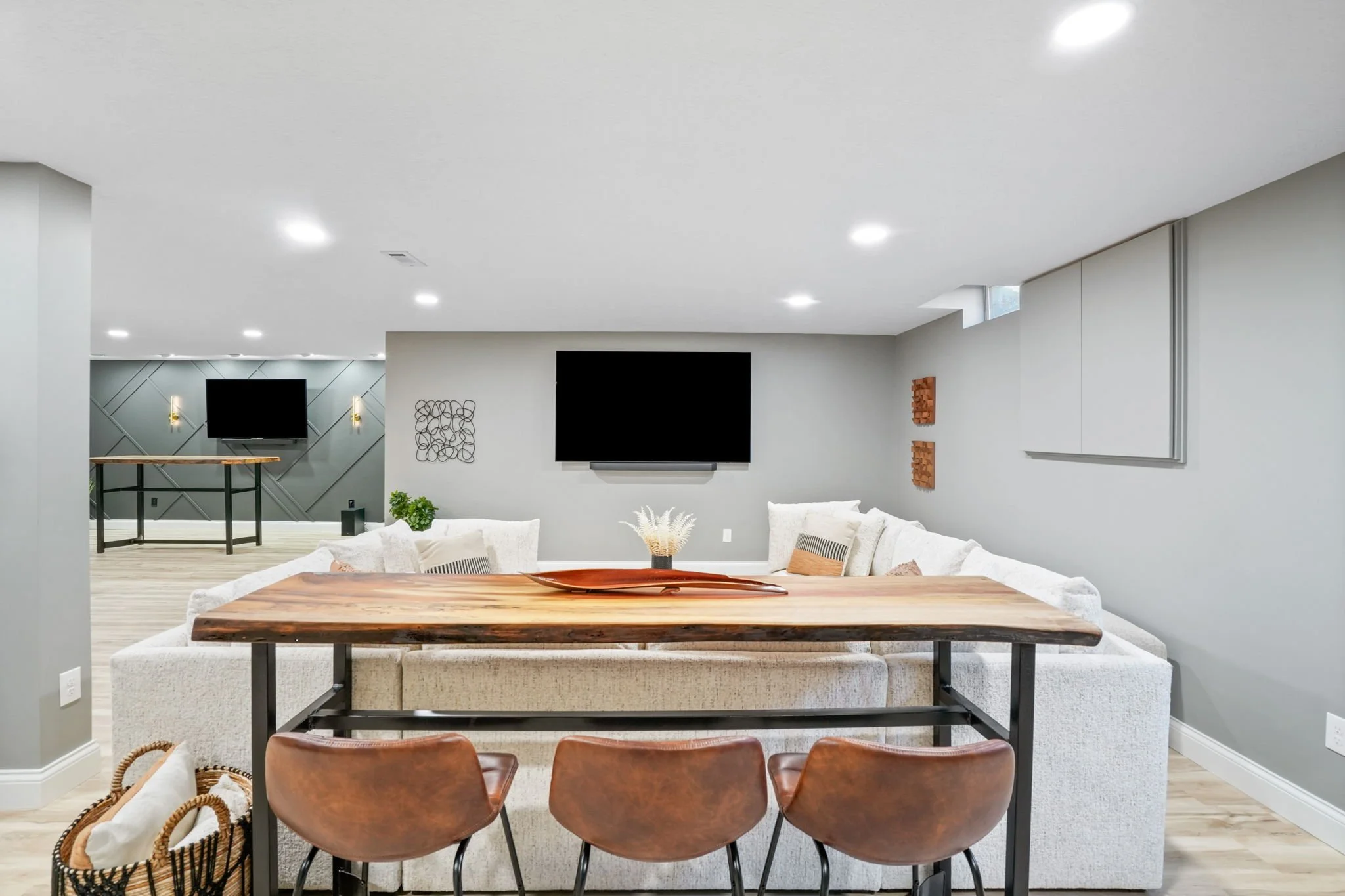 Living room with television, sectional sofa, wooden dining table, three brown chairs, wall decor, and modern lighting