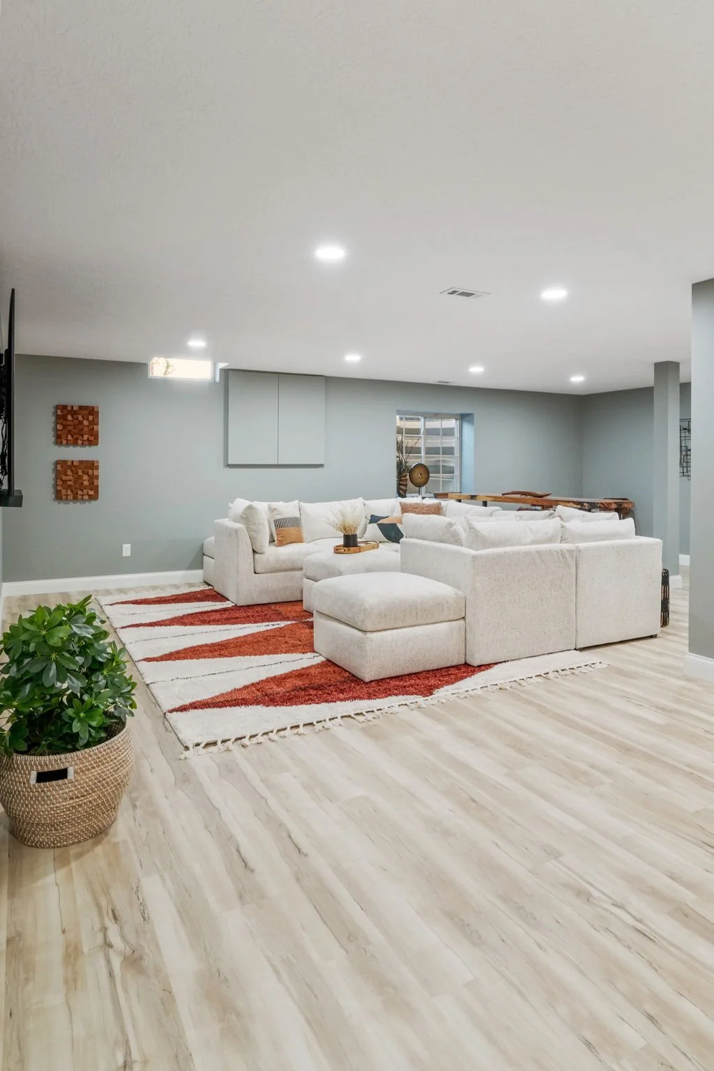 Living room with a white sectional sofa, a colorful area rug, a potted plant, and decorative items, with a blue-gray wall and ceiling lights.