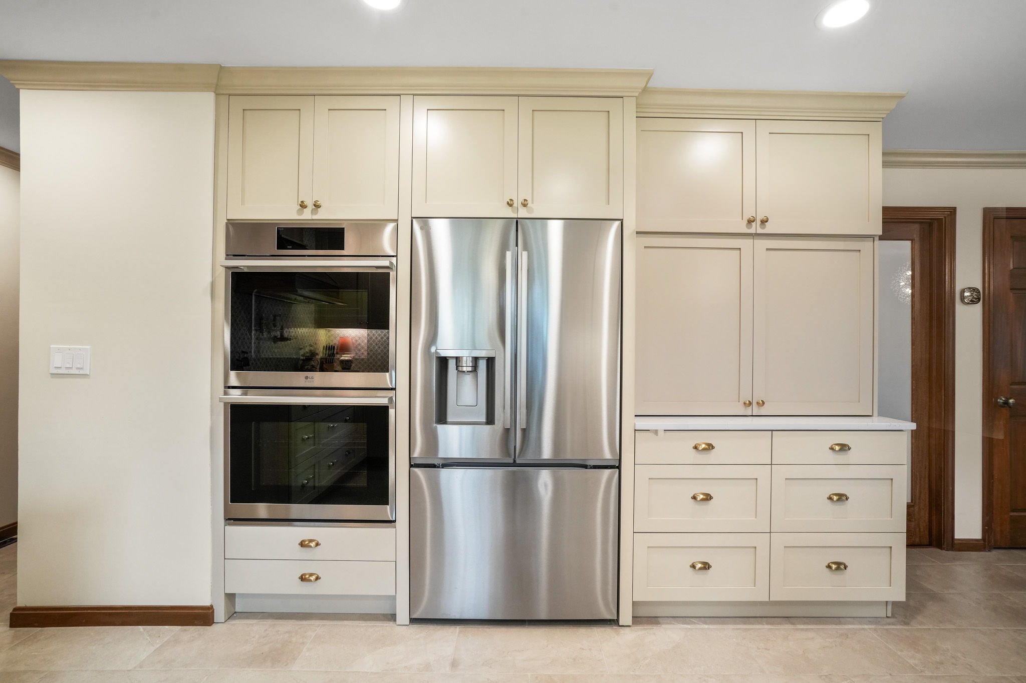 Kitchen with beige cabinets, a stainless steel refrigerator, and built-in oven, with hardwood trim and beige tile floor.
