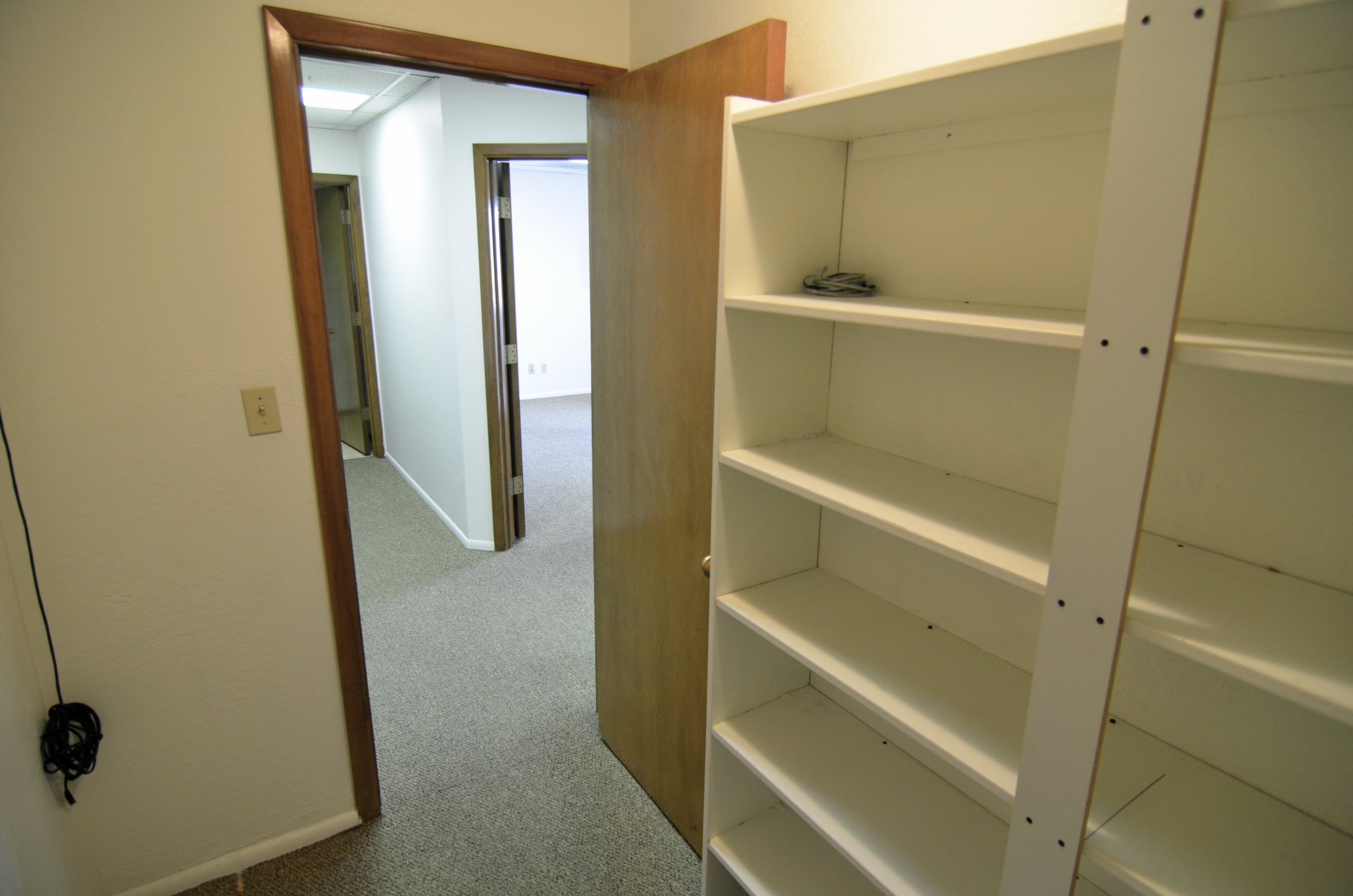 Empty white bookshelf in a room with beige walls and a corridor with an open door.