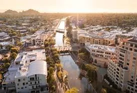 Aerial view of a cityscape with buildings, a waterway, and a bridge at sunset.