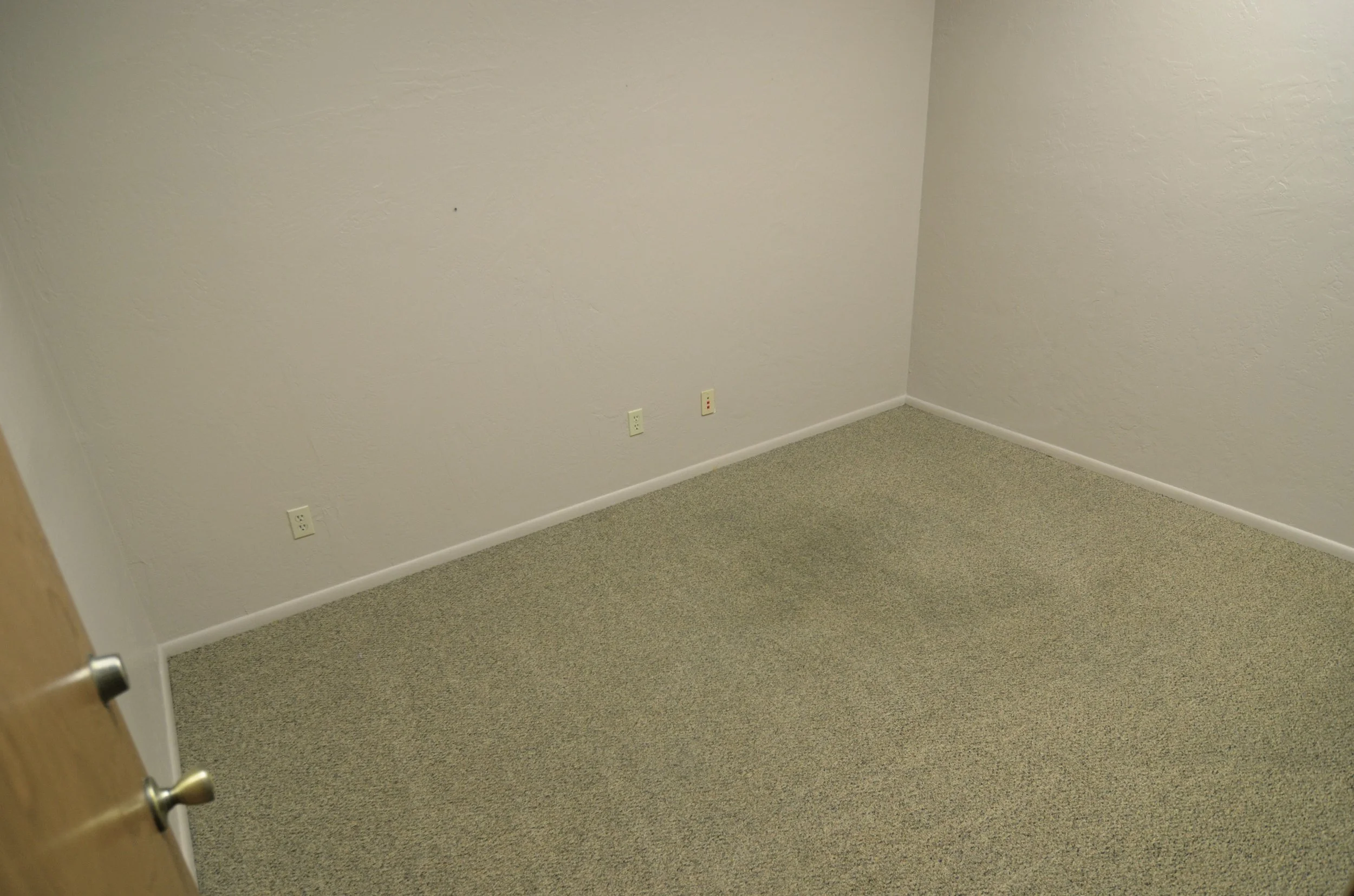 Empty beige-walled room with electrical outlets and a door frame visible on the left side.