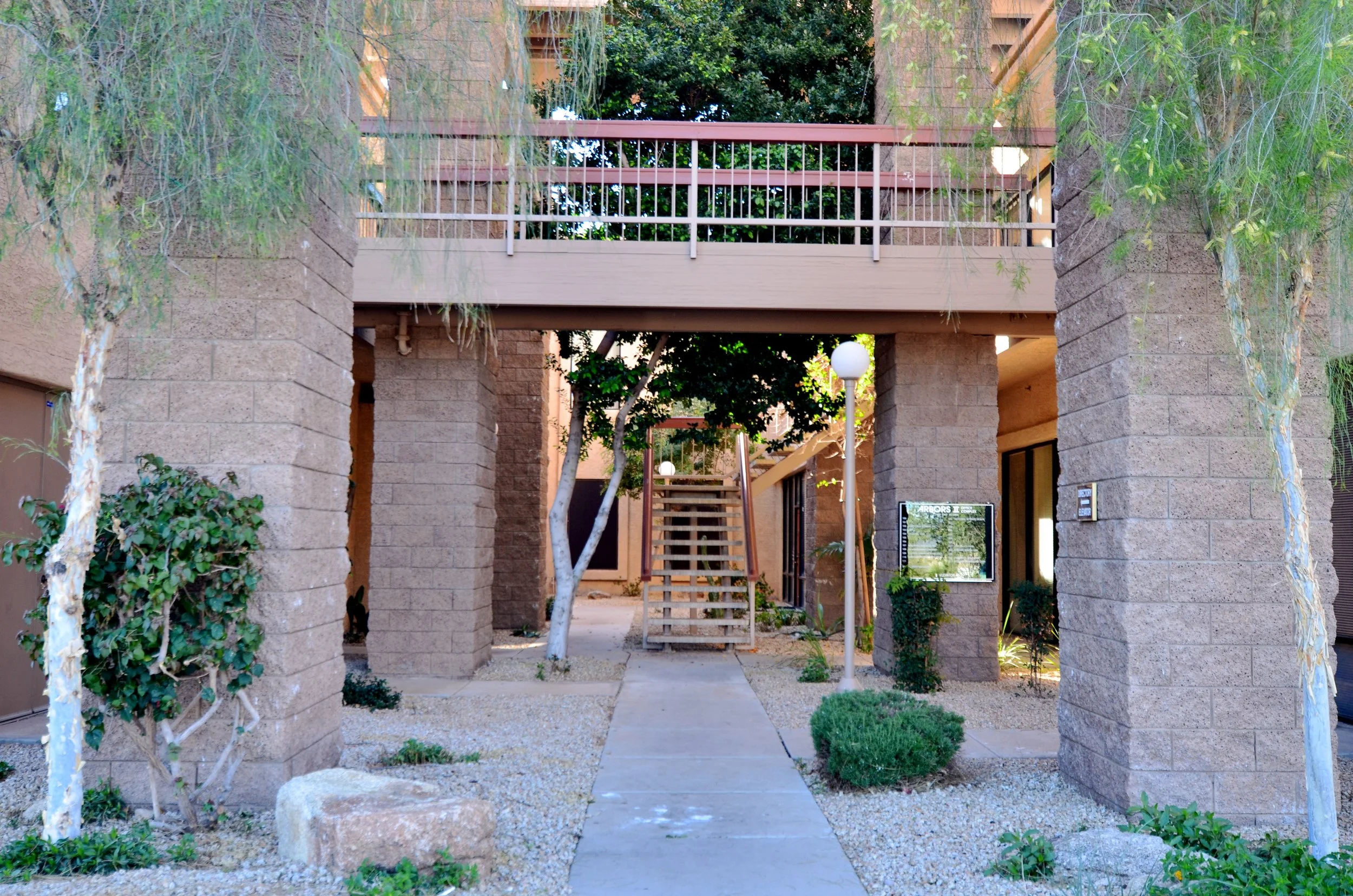 An apartment complex courtyard with stone pillars, trees, a staircase, and outdoor lighting fixtures.