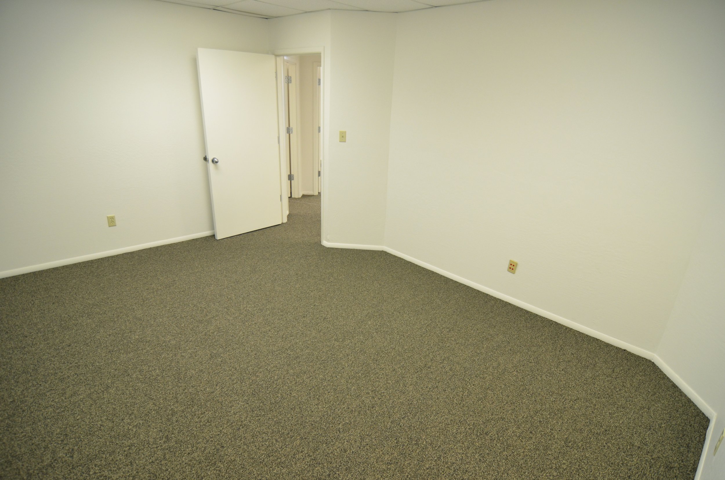 Empty room with beige carpet, white walls, and open door leading to hallway with additional doors.