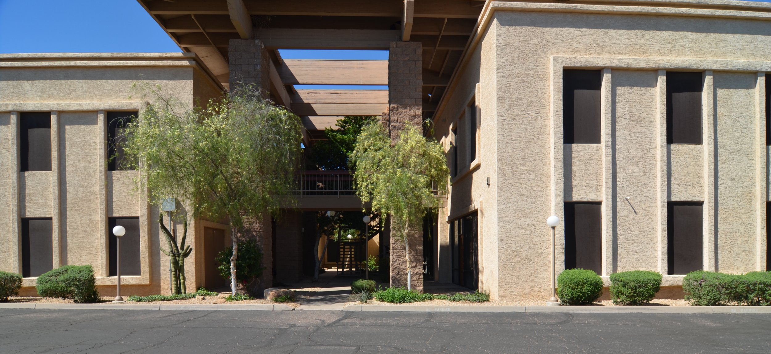 Apartment building with a central sign entrance, trees, shrubs, and pathway, under construction with exposed wooden beams