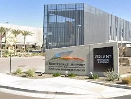 Modern glass building with a sign for Volant Contemporary & Luxury, located in Scottsdale Airpark, with palm trees and a clear sky