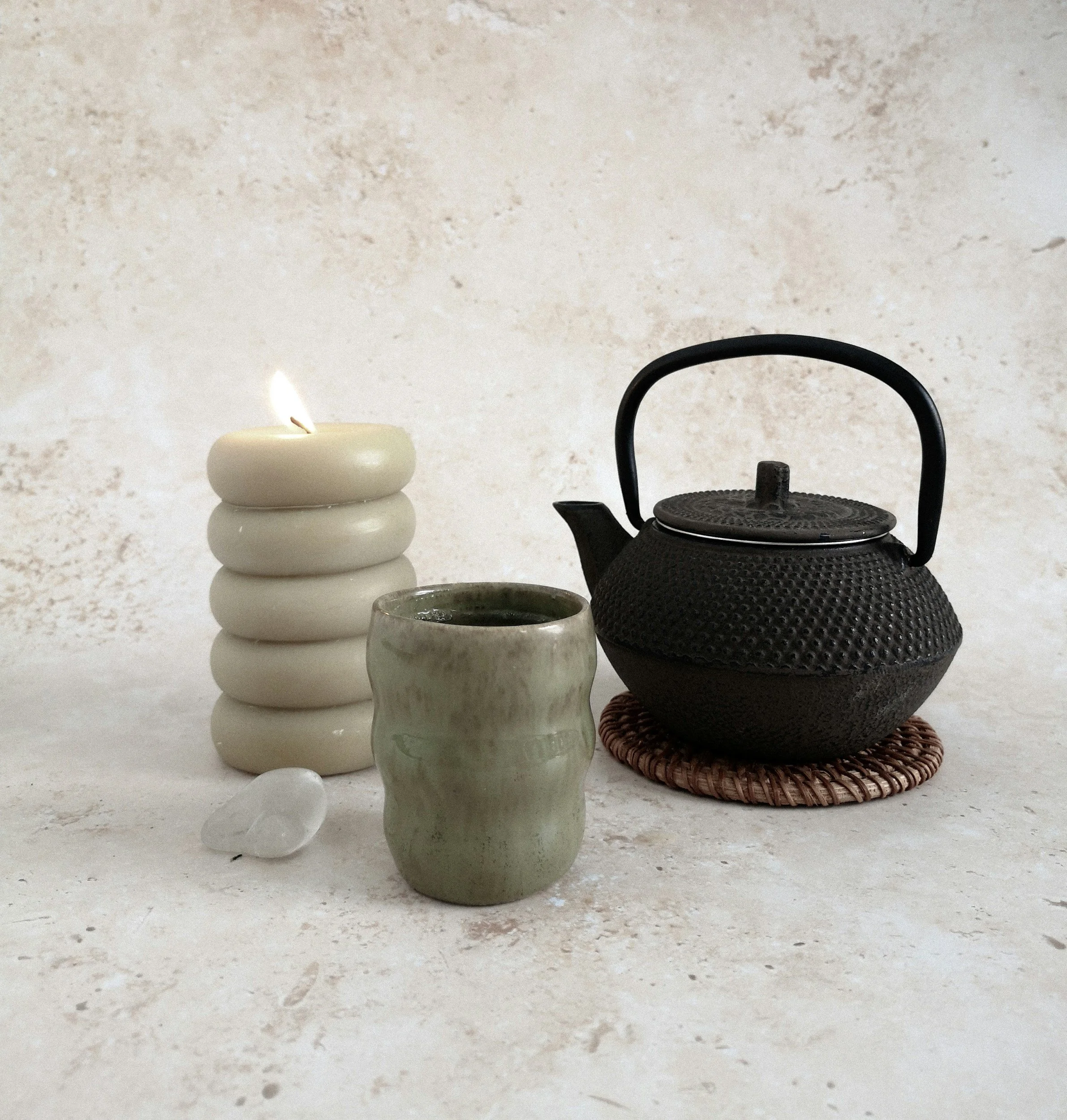 Schwarze Teekanne, grüne Tasse, weiße Kerze, kleine Welle aus Quarz, auf heller Oberfläche und Hintergrund.