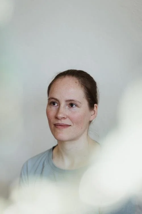 Porträt einer jungen Frau mit braunen Haaren und einem blauen T-Shirt, die auf einen Punkt außerhalb des Bildes schaut.