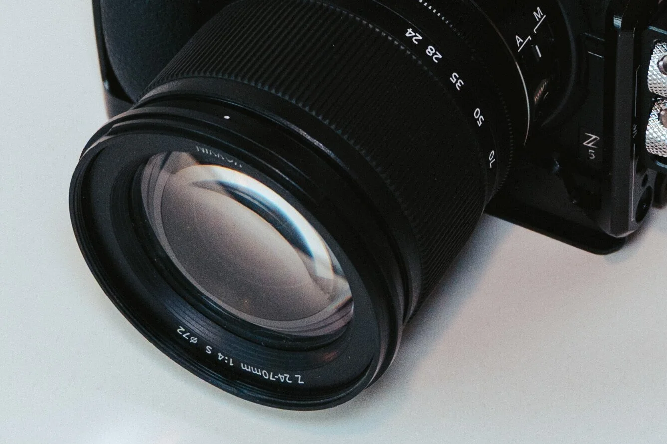 Close-up of a camera with a large zoom lens, placed on a white surface.