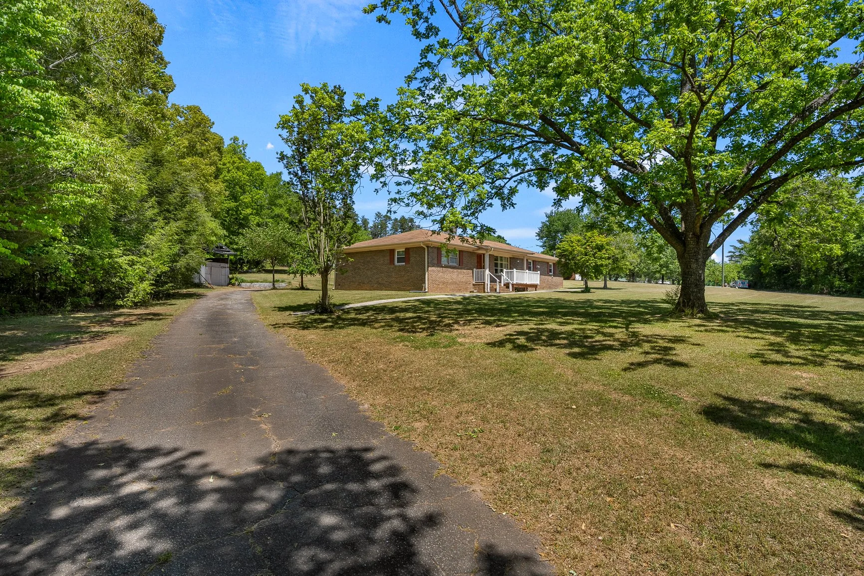 Long driveway approach to brick home with attached garage and established landscaping.