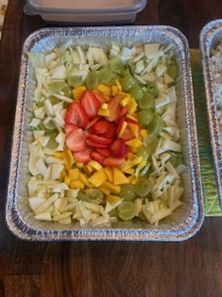 A foil tray filled with chopped celery, grapes, strawberries, and mango slices.